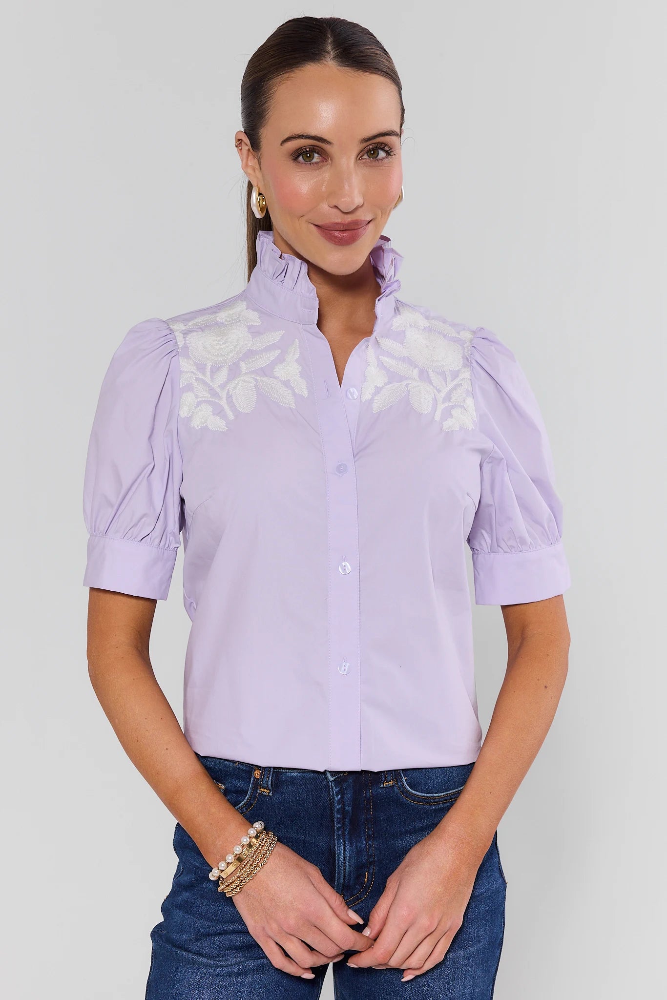 Woman wearing a light purple blouse with lace details on a plain background
