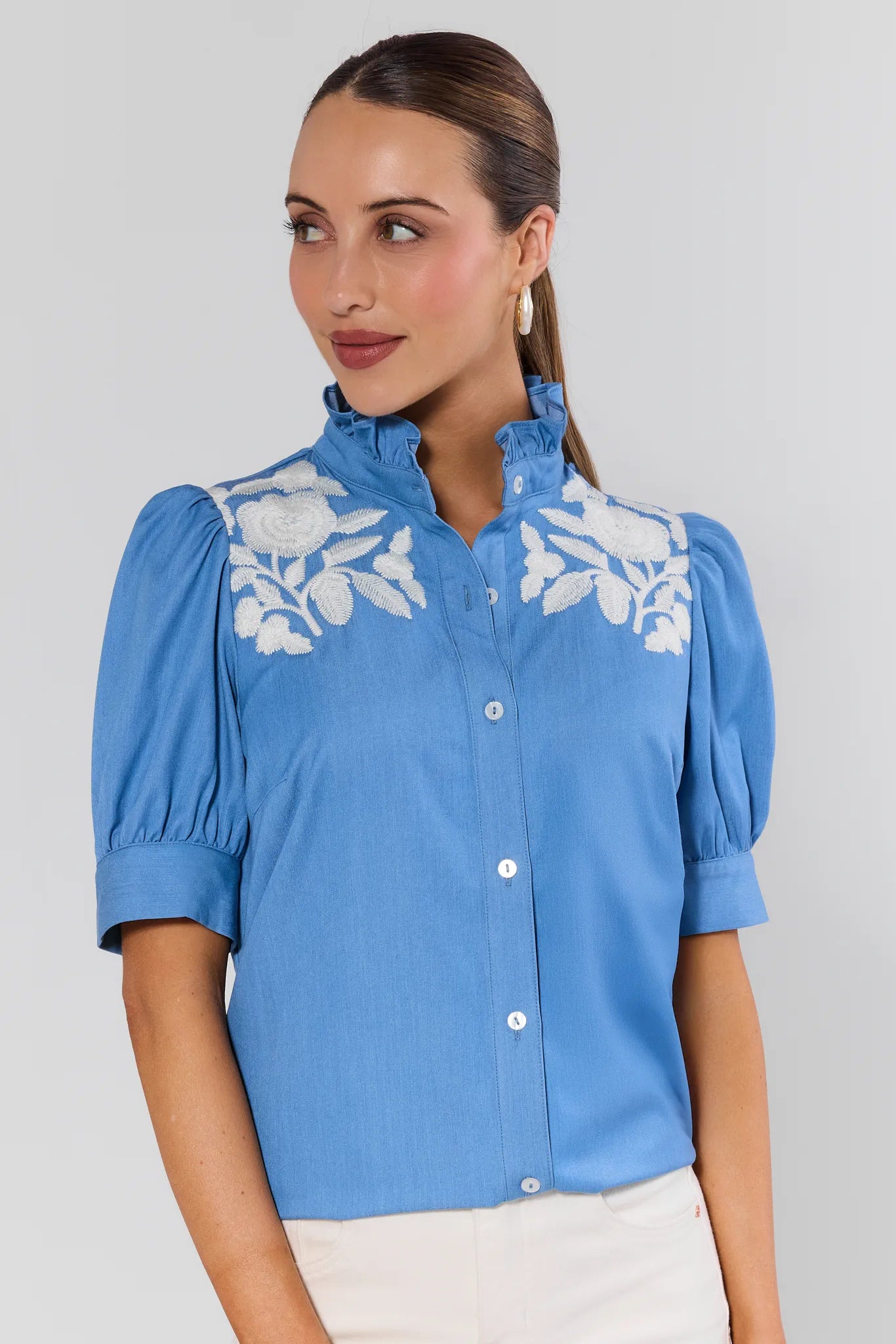 Woman wearing a blue blouse with white floral embroidery on a plain background