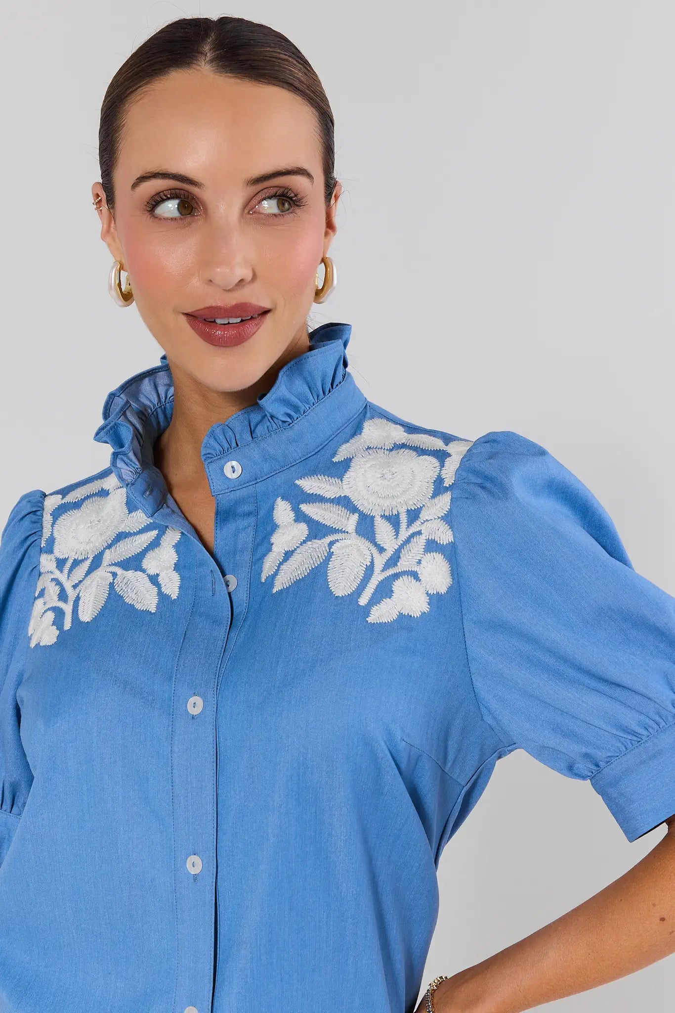 Woman wearing a blue blouse with white floral embroidery on a plain background