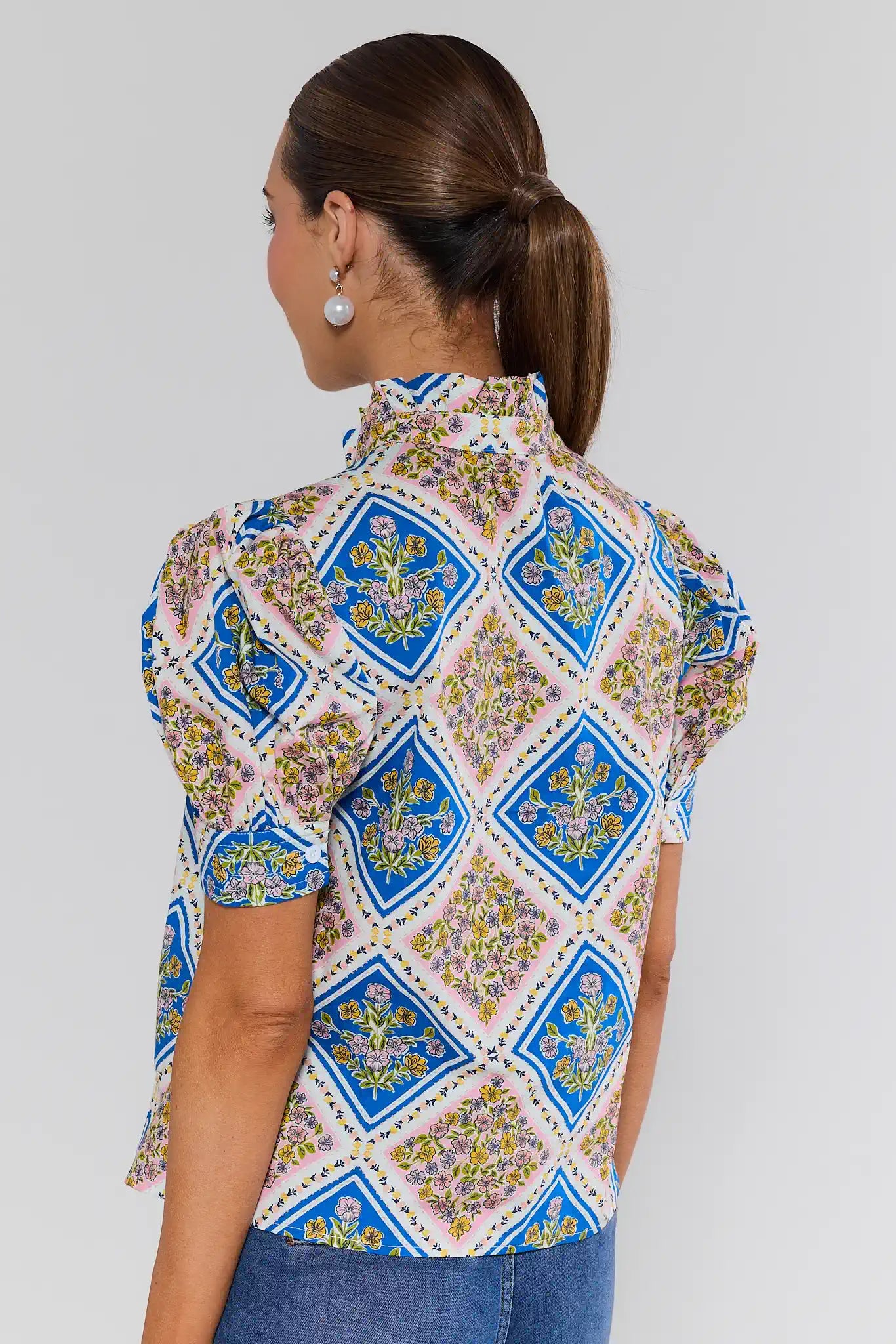 Woman wearing a patterned blouse with blue geometric designs on a plain background