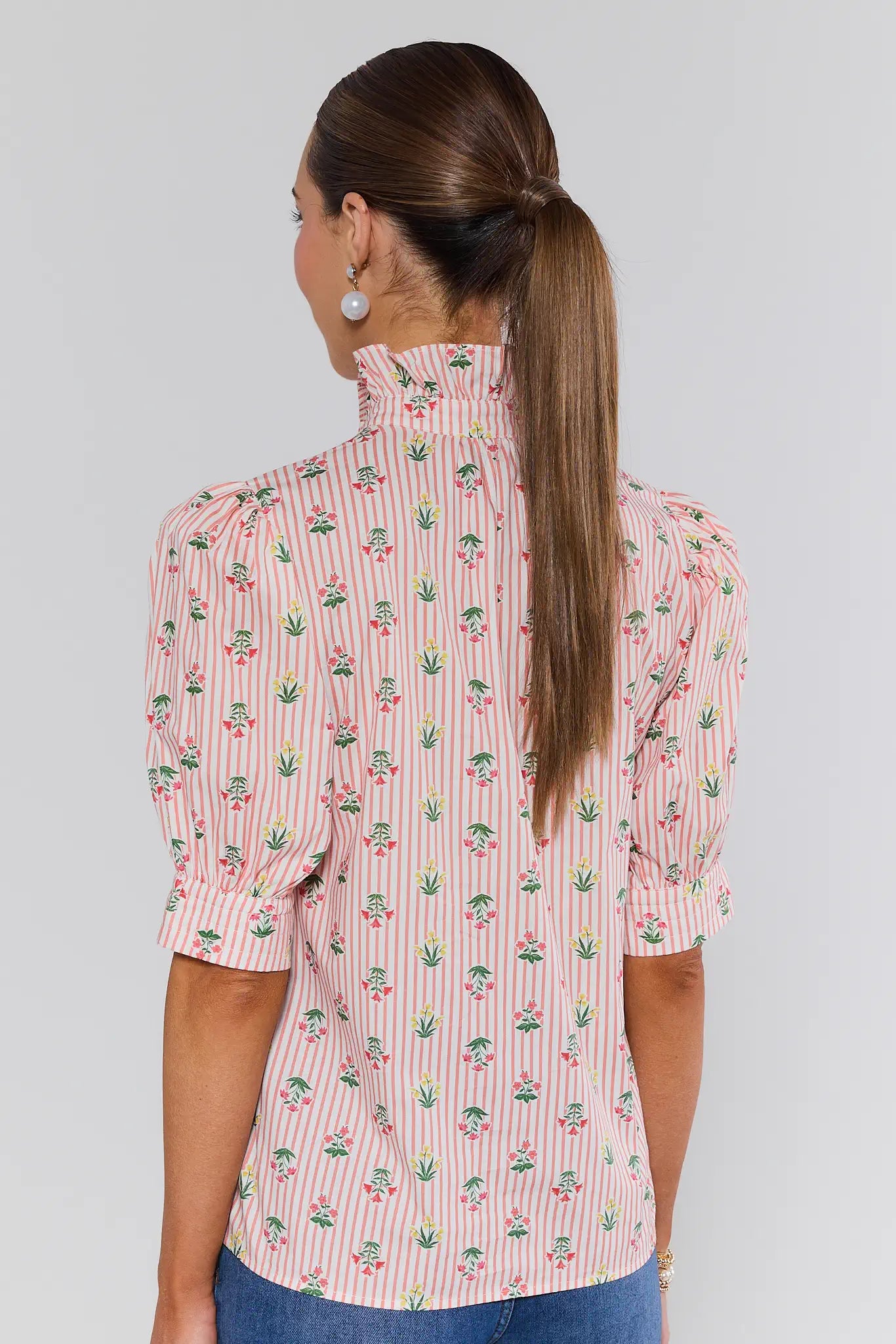 Woman wearing a pink patterned blouse against a gray background