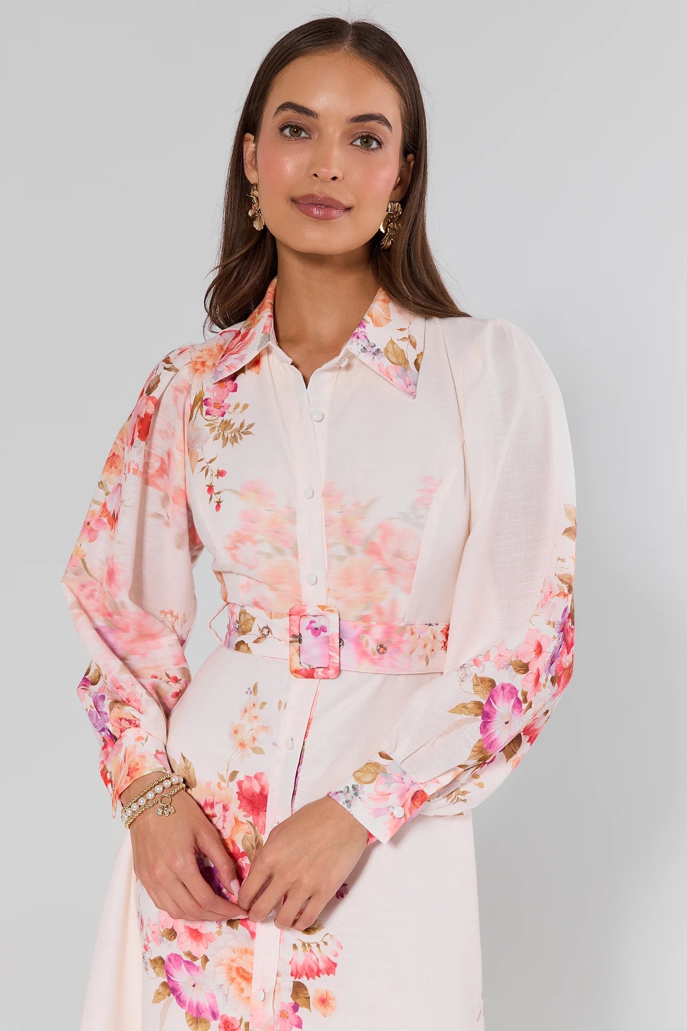 Woman wearing a white blouse with pink floral patterns on a plain background