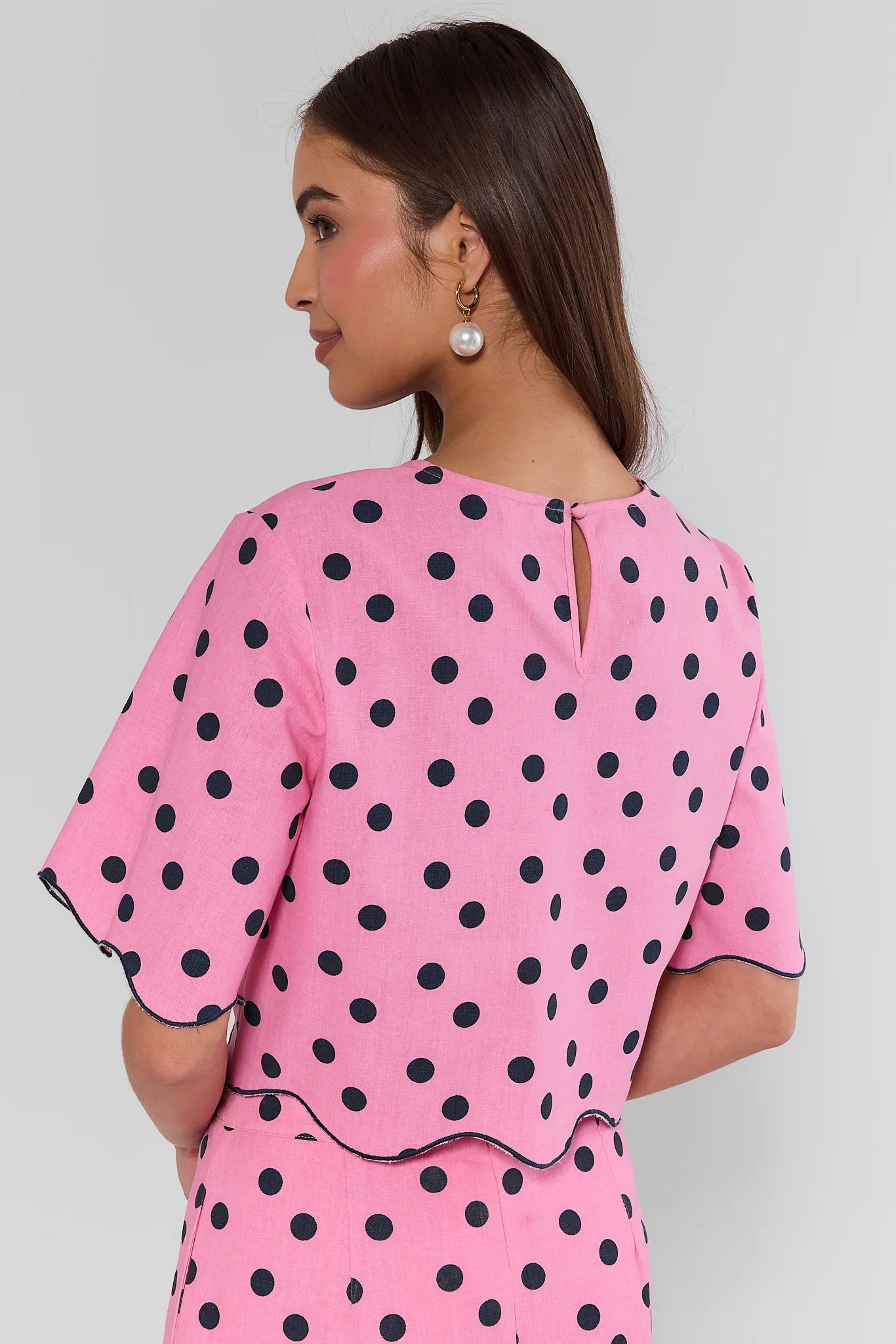 Woman wearing a pink polka dot outfit on a plain background