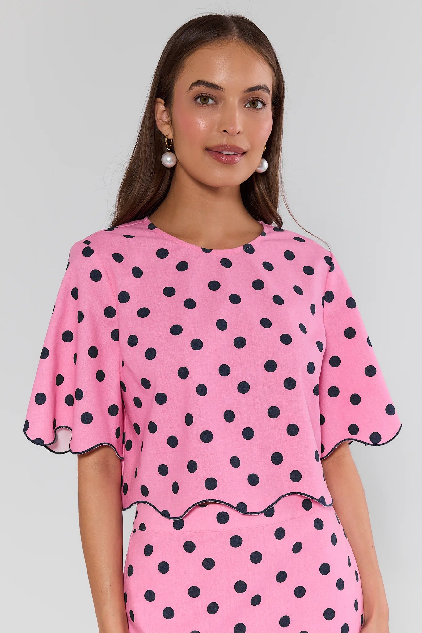 Woman wearing a pink dress with black polka dots against a plain background