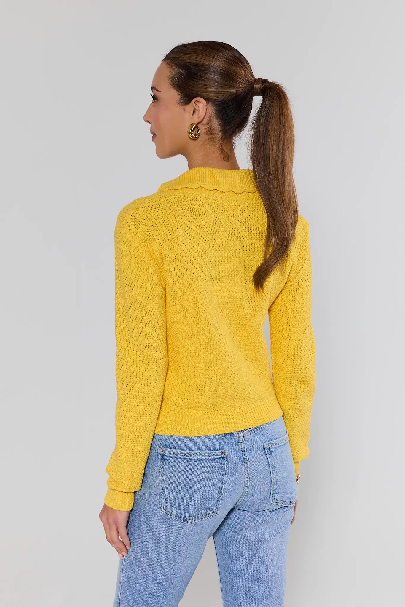 Woman wearing a yellow sweater and blue jeans against a plain background