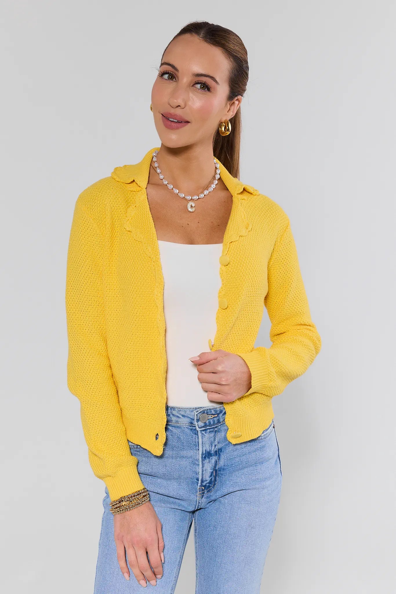 Woman wearing a yellow jacket, white top, and blue jeans against a plain background