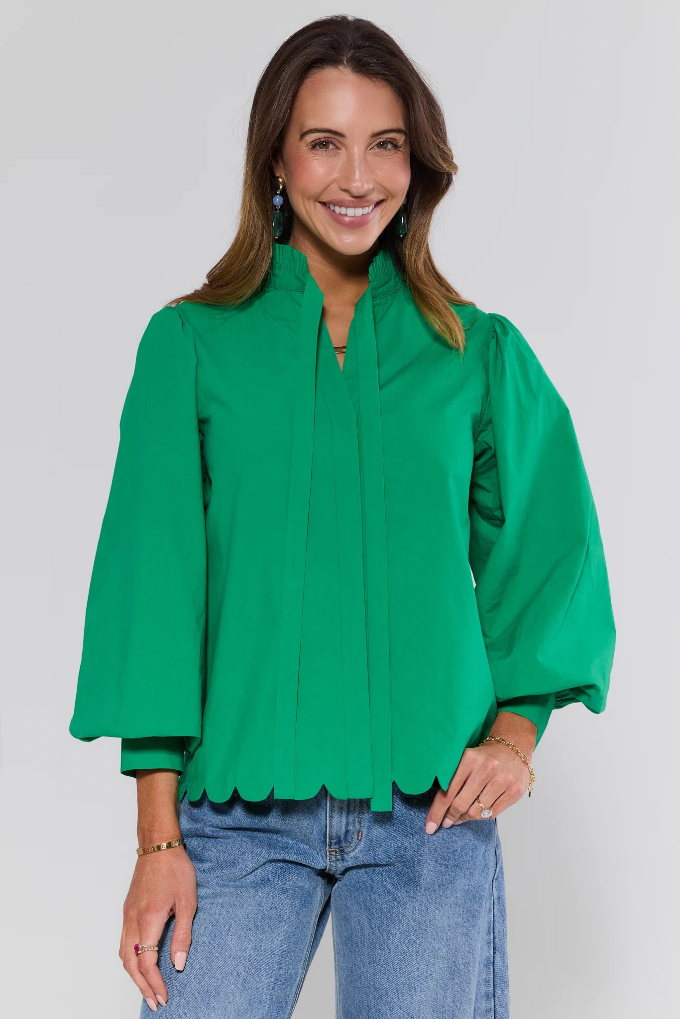 Woman wearing a green blouse with scalloped edges and blue jeans on a white background