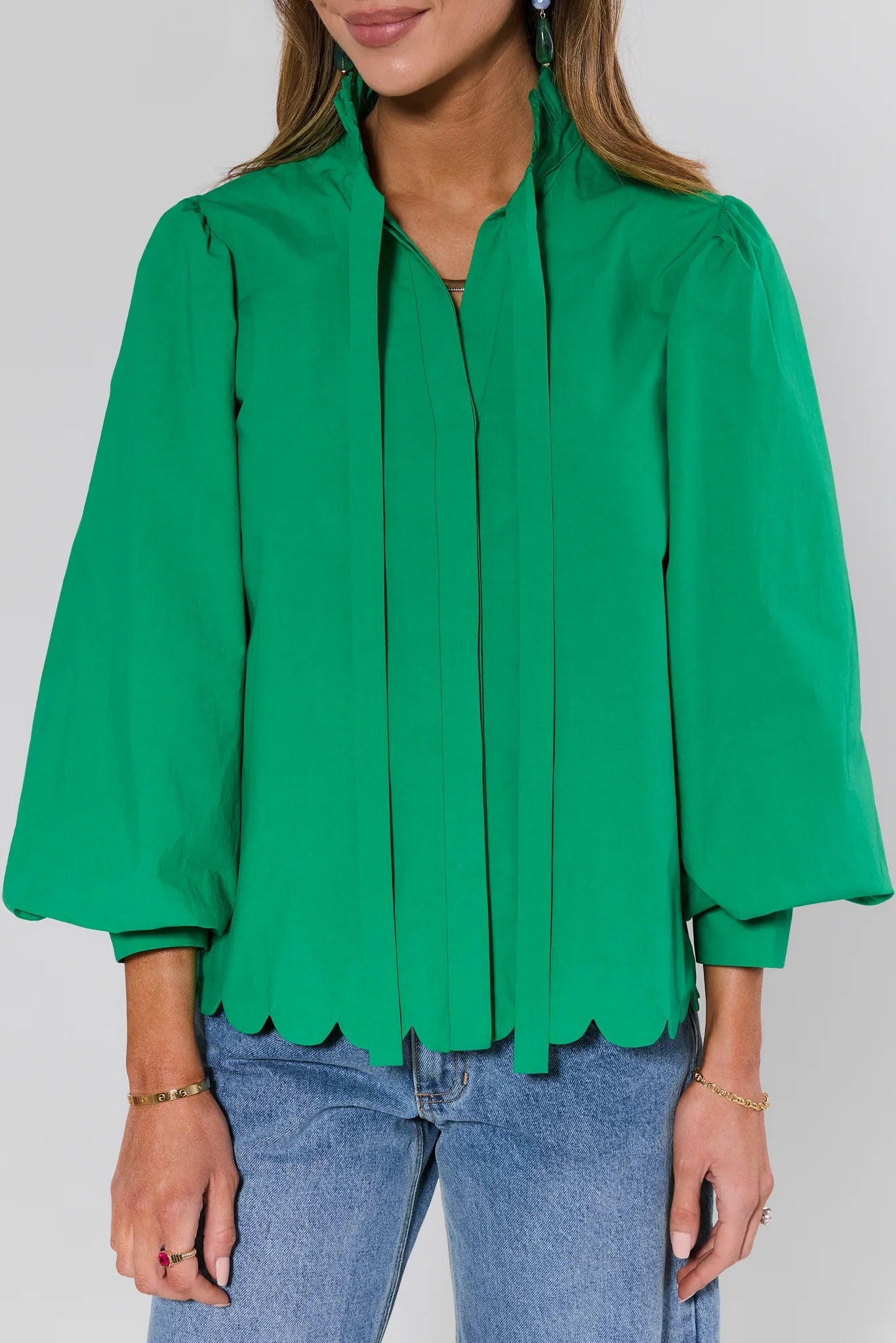 Green blouse with scalloped hem and blue jeans on a plain background