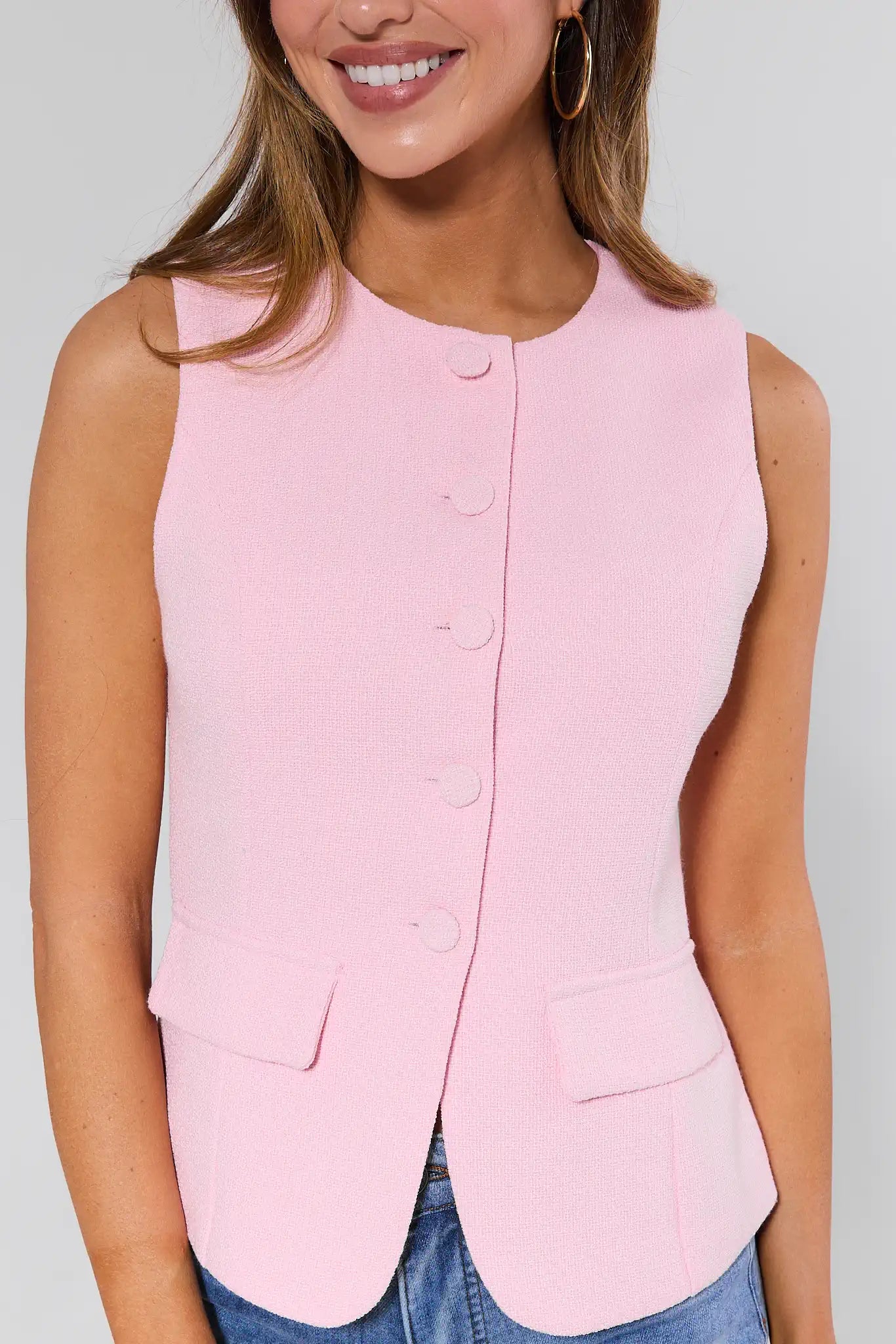 Woman wearing a pink sleeveless blazer against a plain background