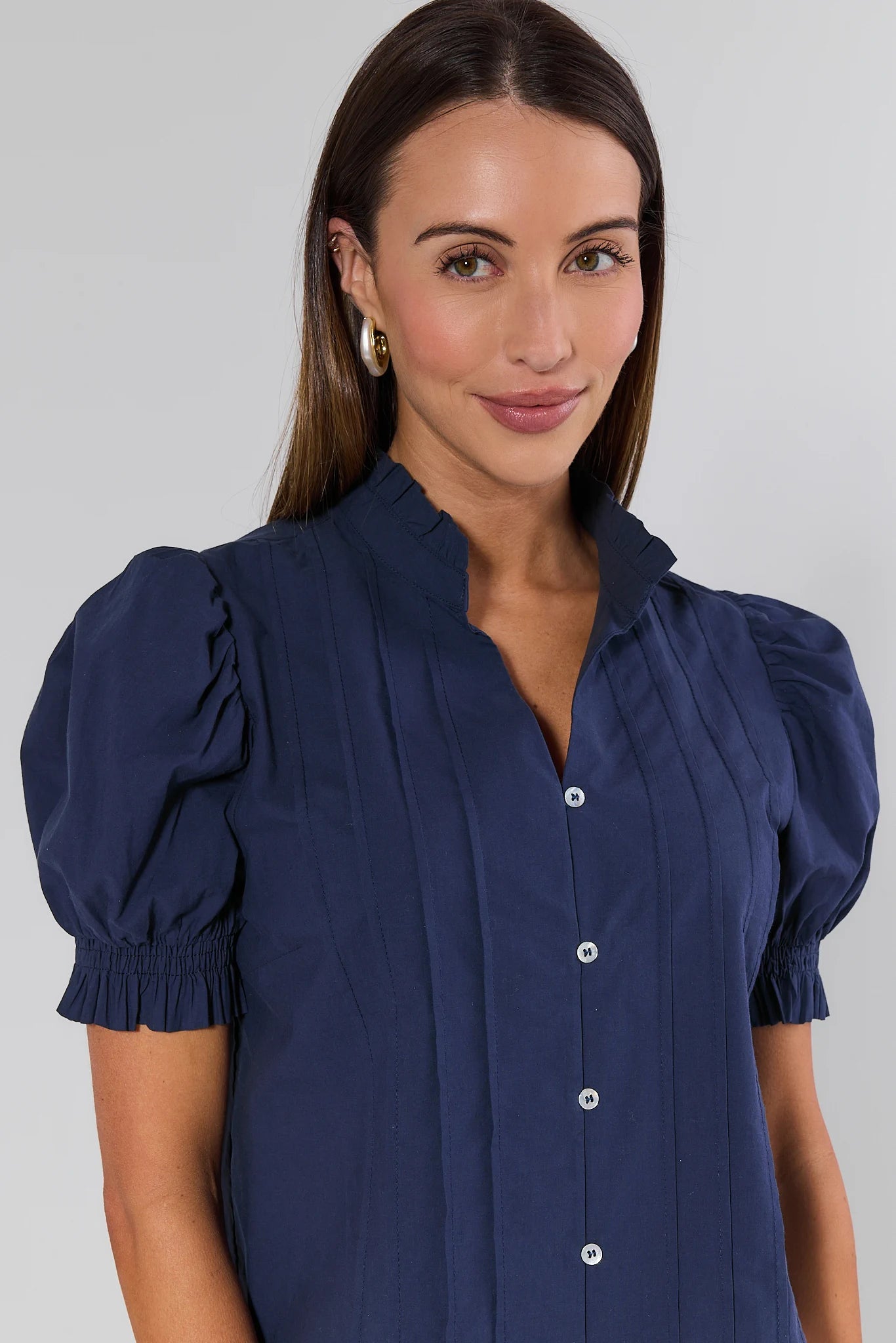 Woman wearing a navy blue blouse with puffed sleeves against a gray background
