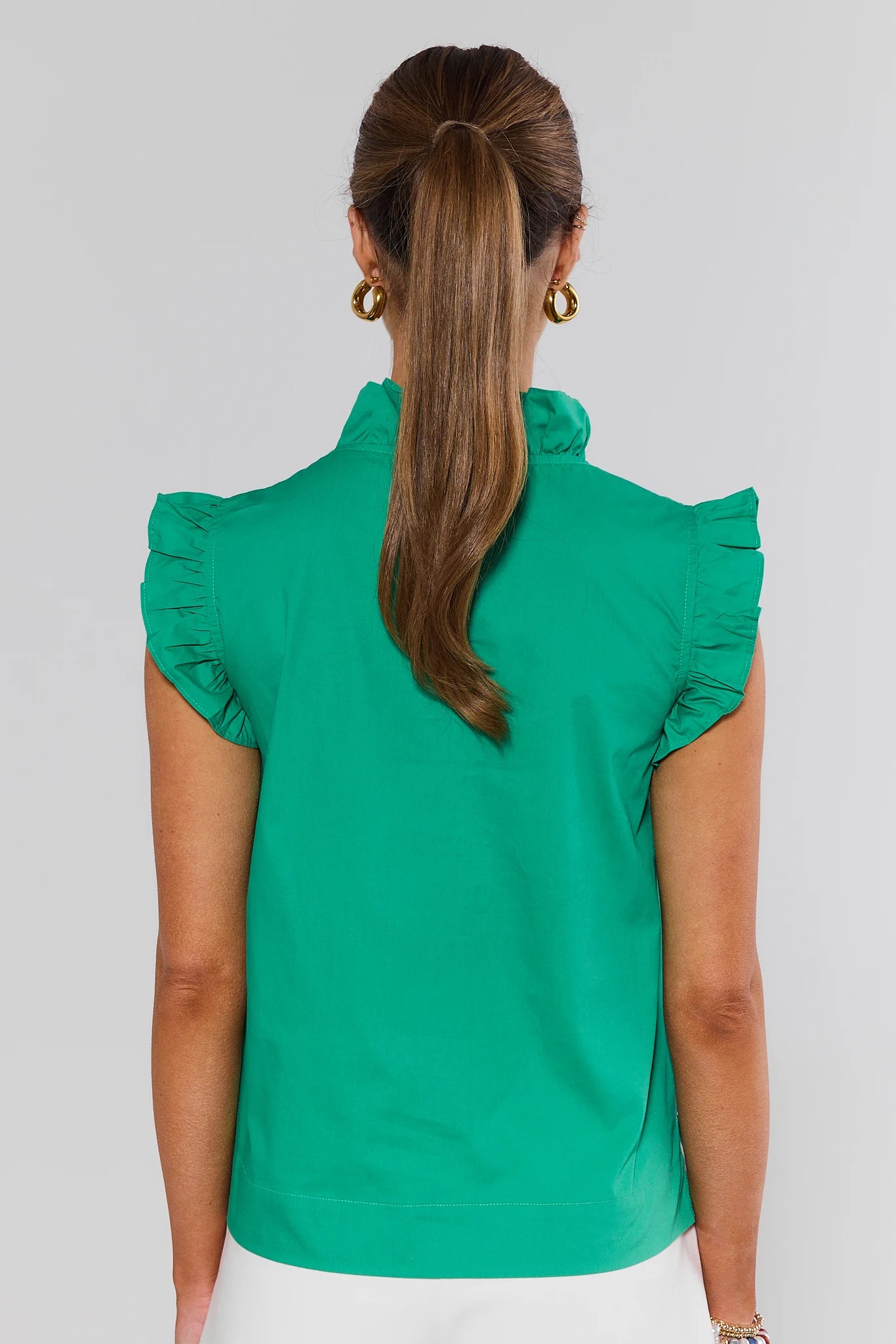 Person wearing a green blouse with ruffled shoulders on a plain background