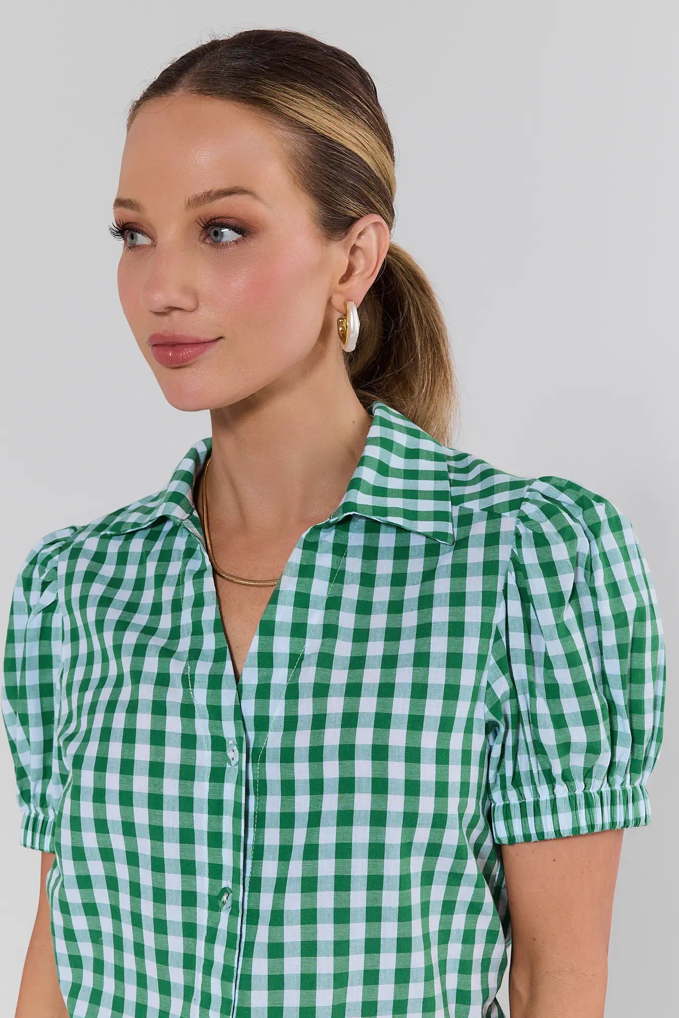 Woman wearing a green and white checkered shirt against a plain background