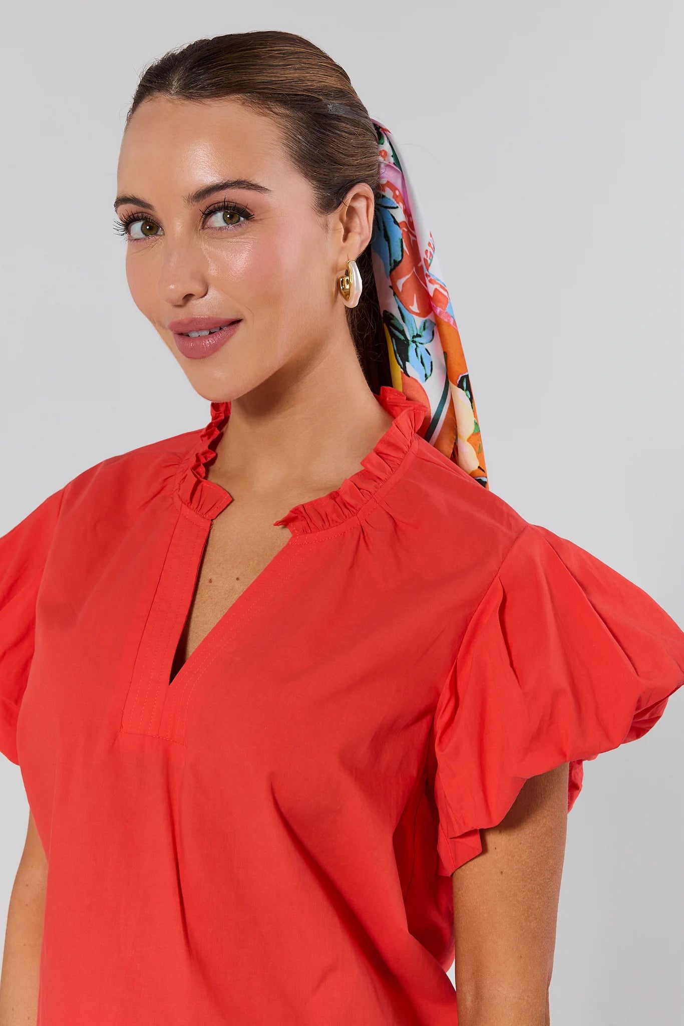 Woman wearing a red blouse with ruffled sleeves and a colorful headscarf on a plain background