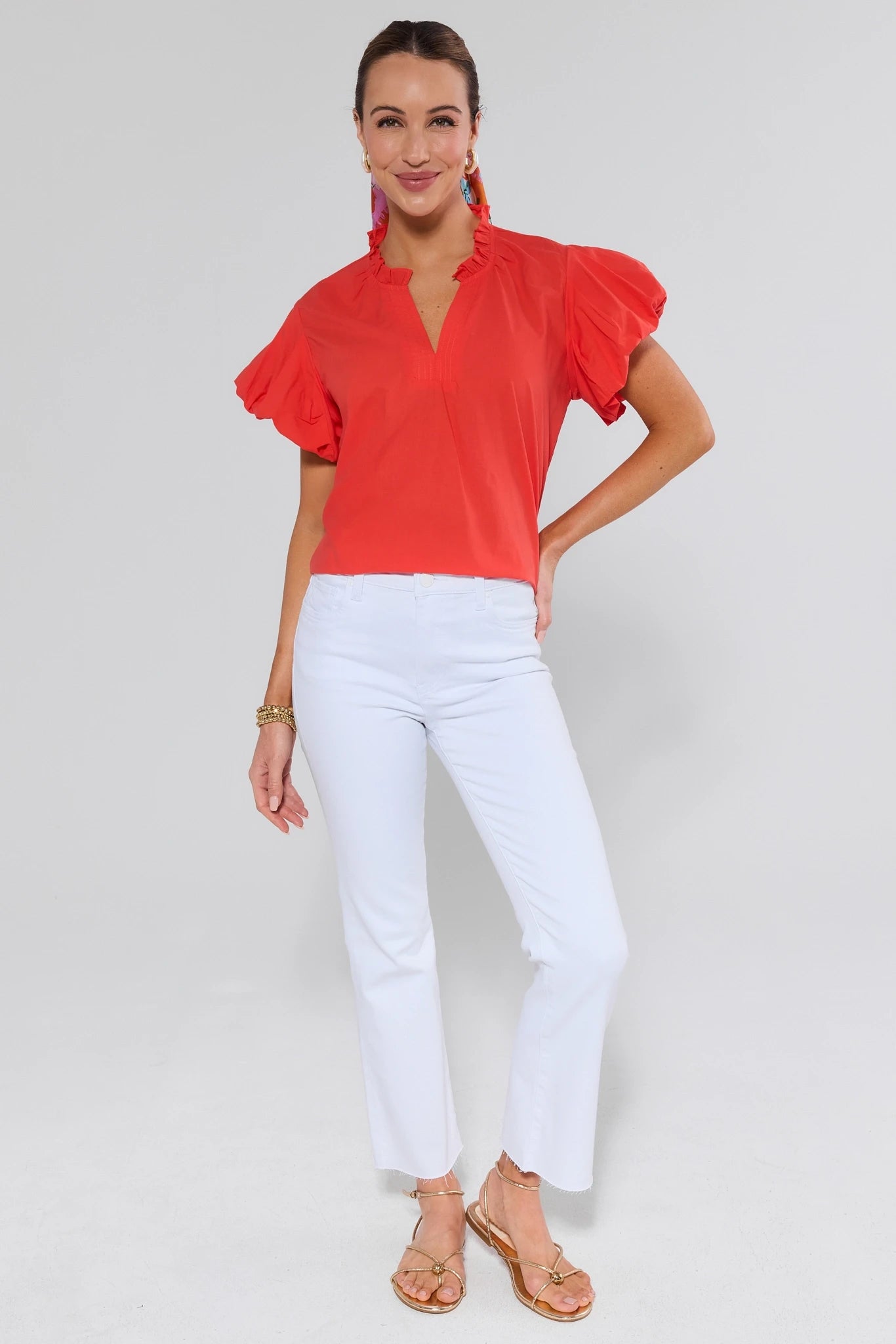 Woman wearing a red blouse with ruffled sleeves and white pants on a plain background