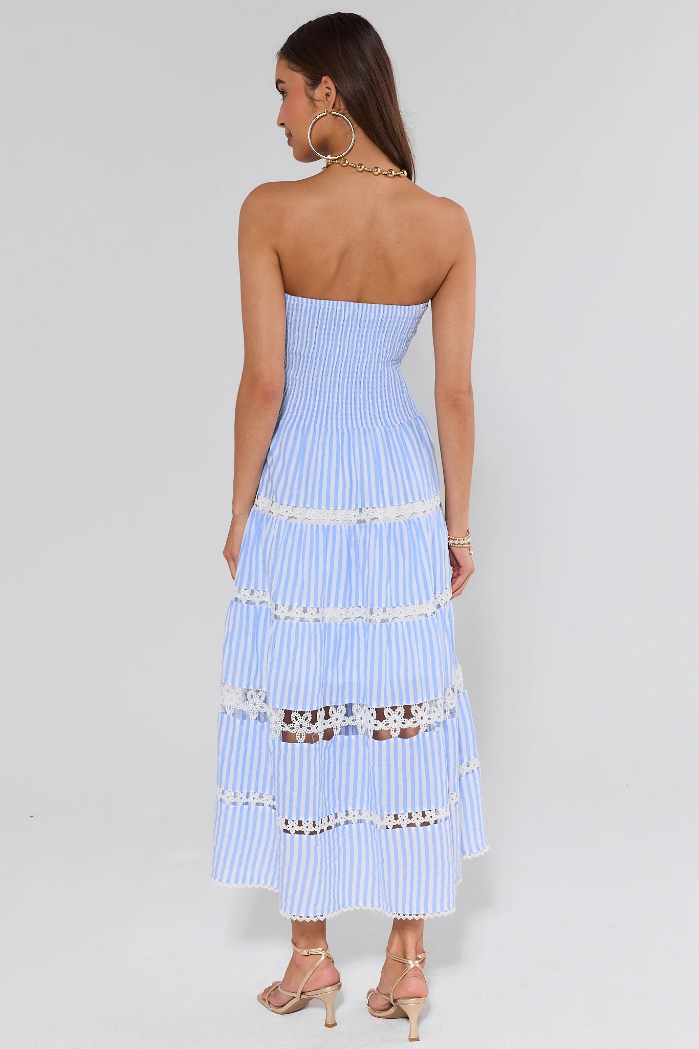 Woman wearing a light blue strapless dress with white stripes and embellishments on a plain background