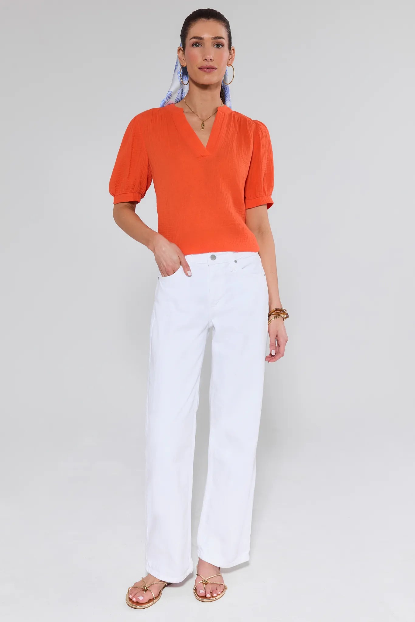 Woman wearing an orange blouse and white pants on a plain background