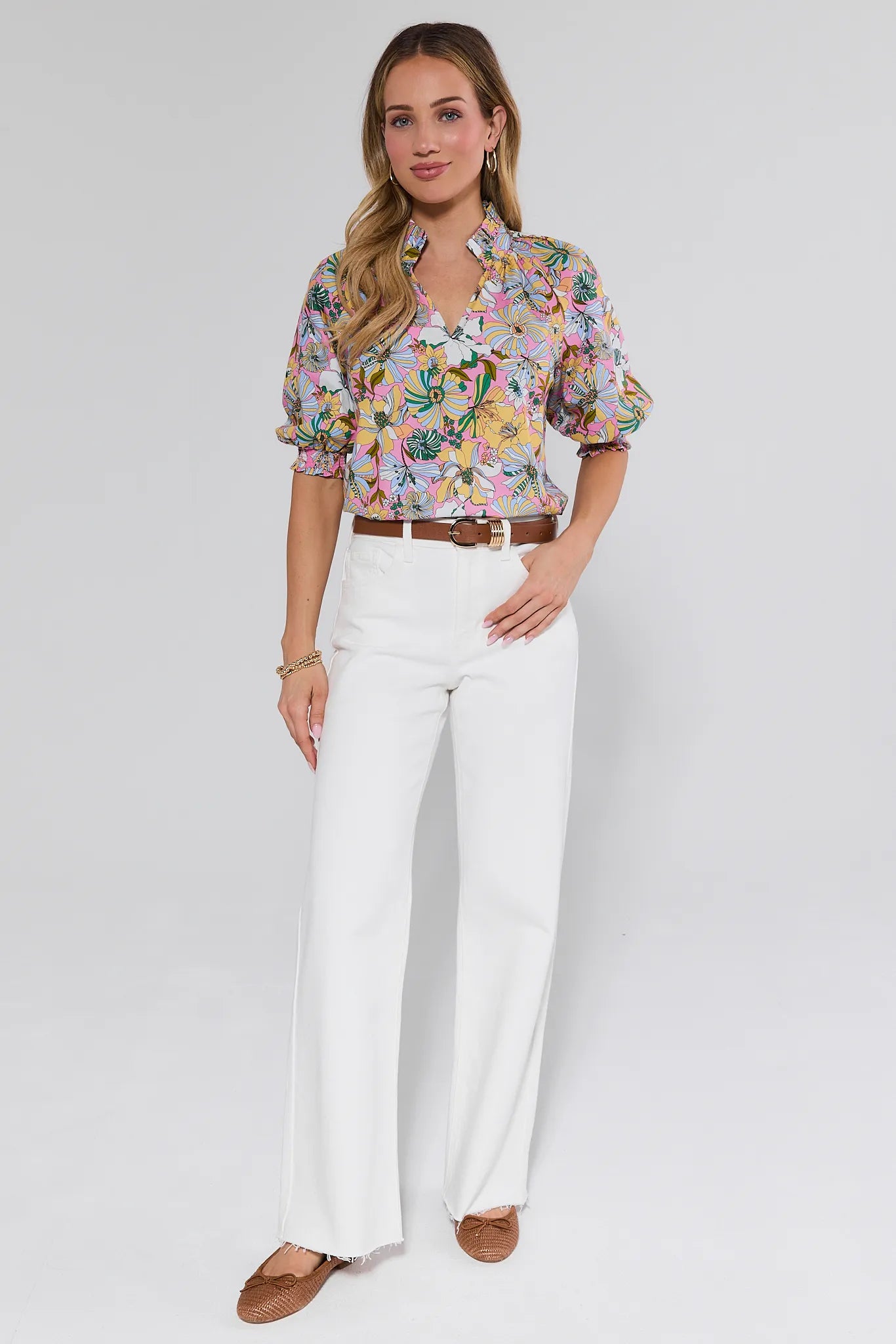 Woman wearing a floral blouse and white pants on a plain background