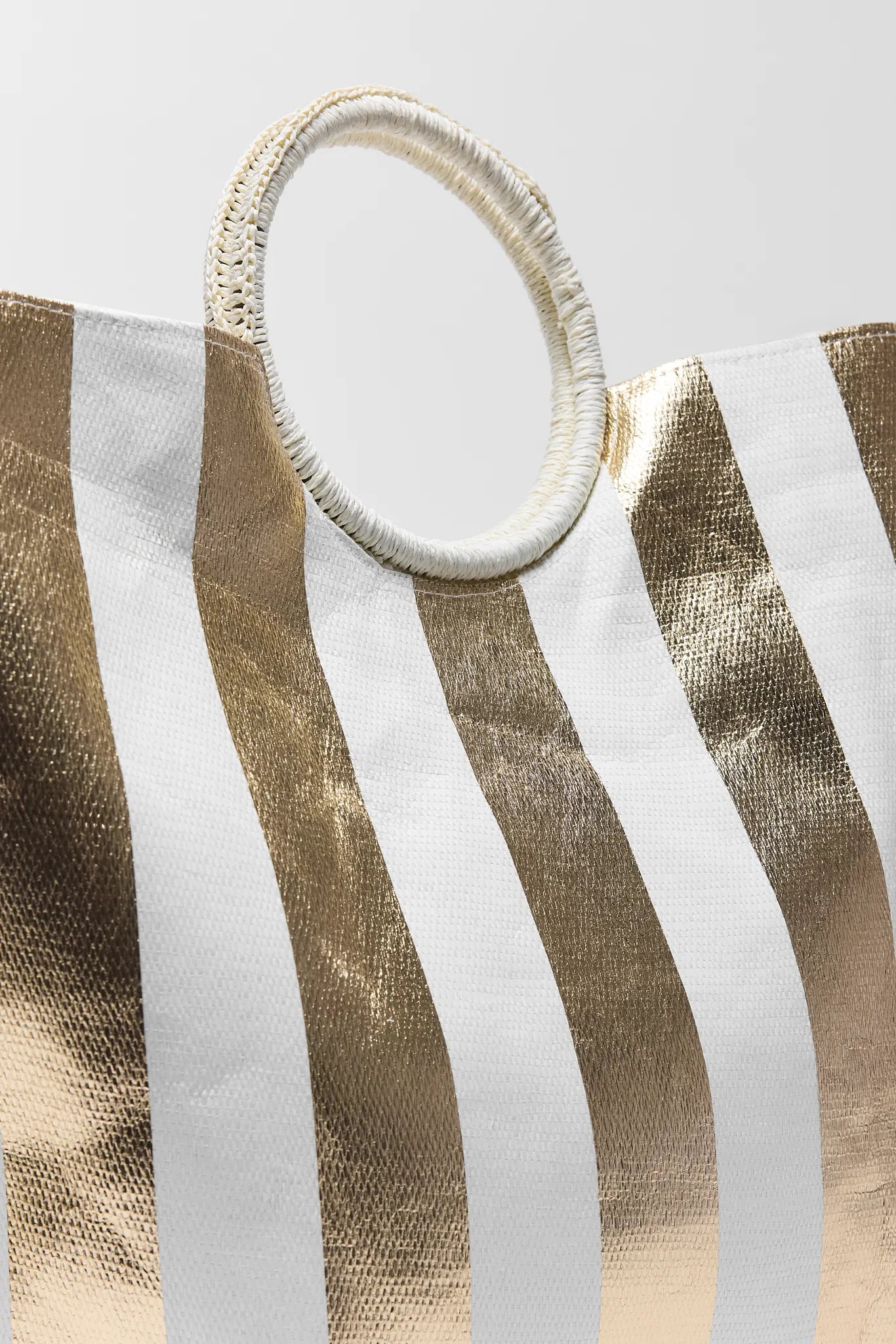Close-up of a gold and white striped Maurice Tote with a woven handle on a light gray background