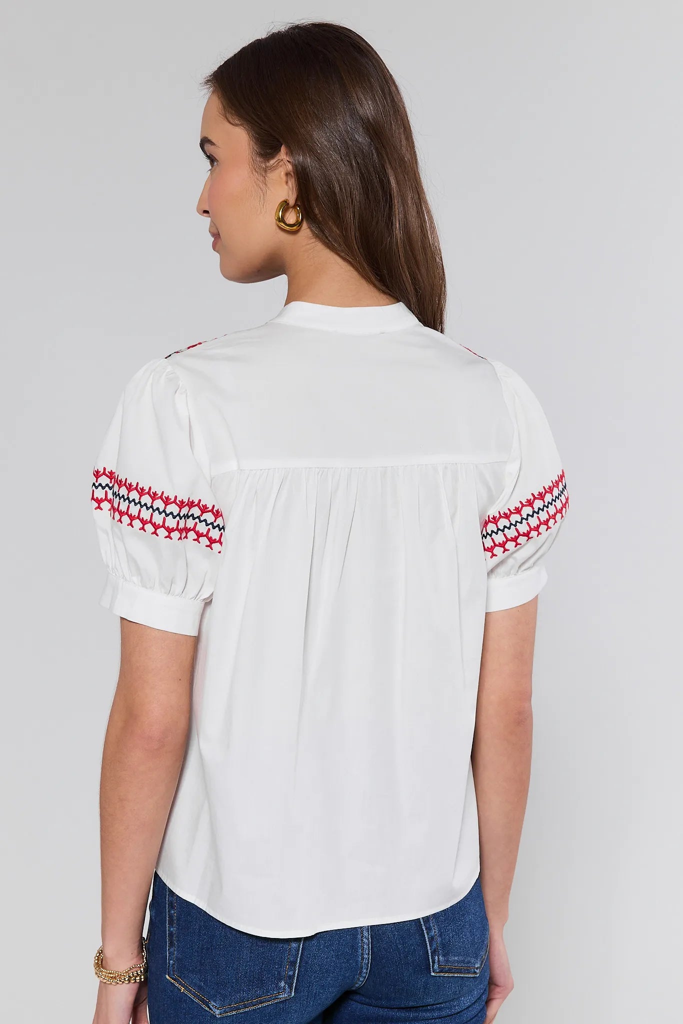 Woman wearing a white blouse with red and black patterns on sleeves against a gray background