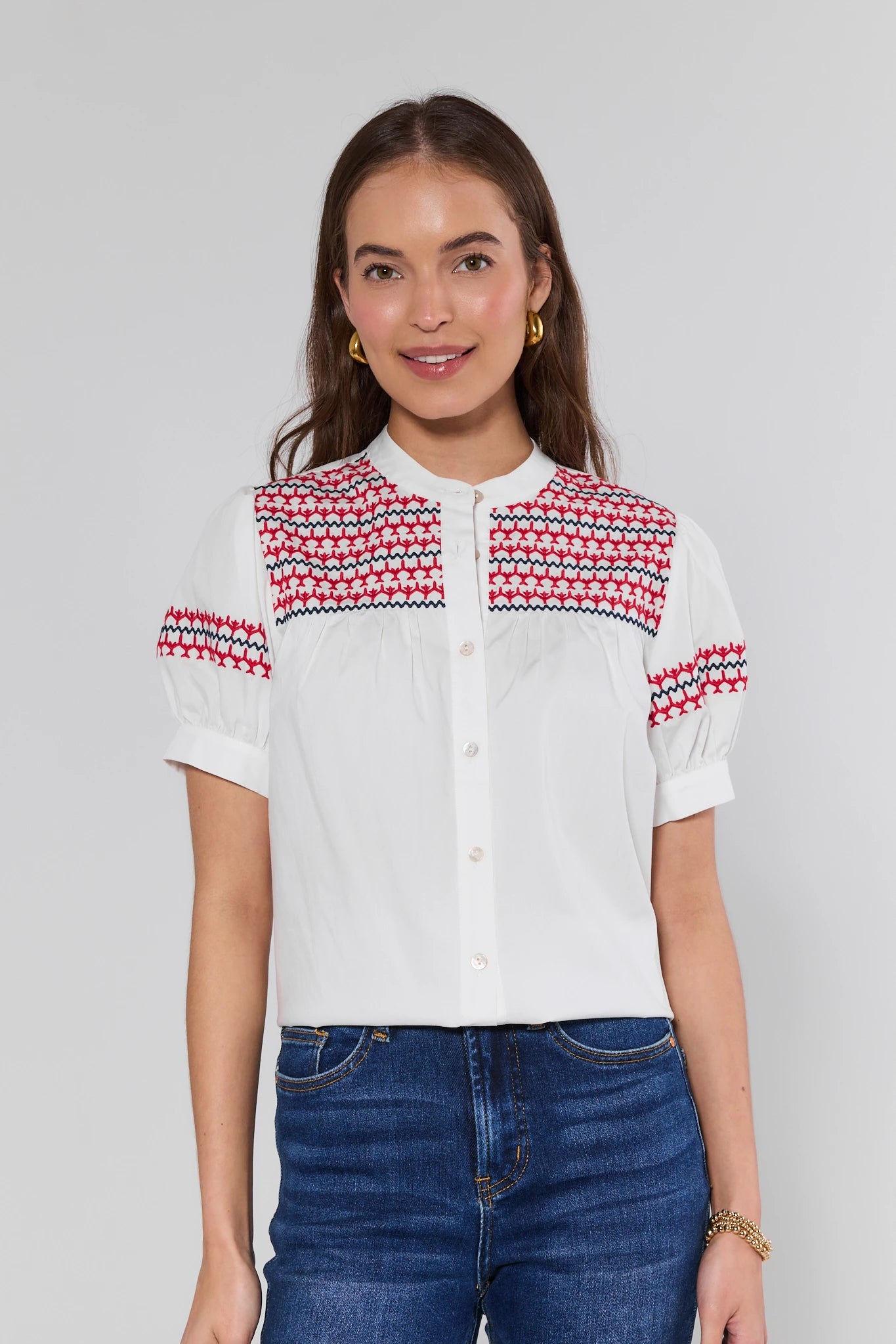Woman wearing a white blouse with red and blue patterned shoulders against a gray background
