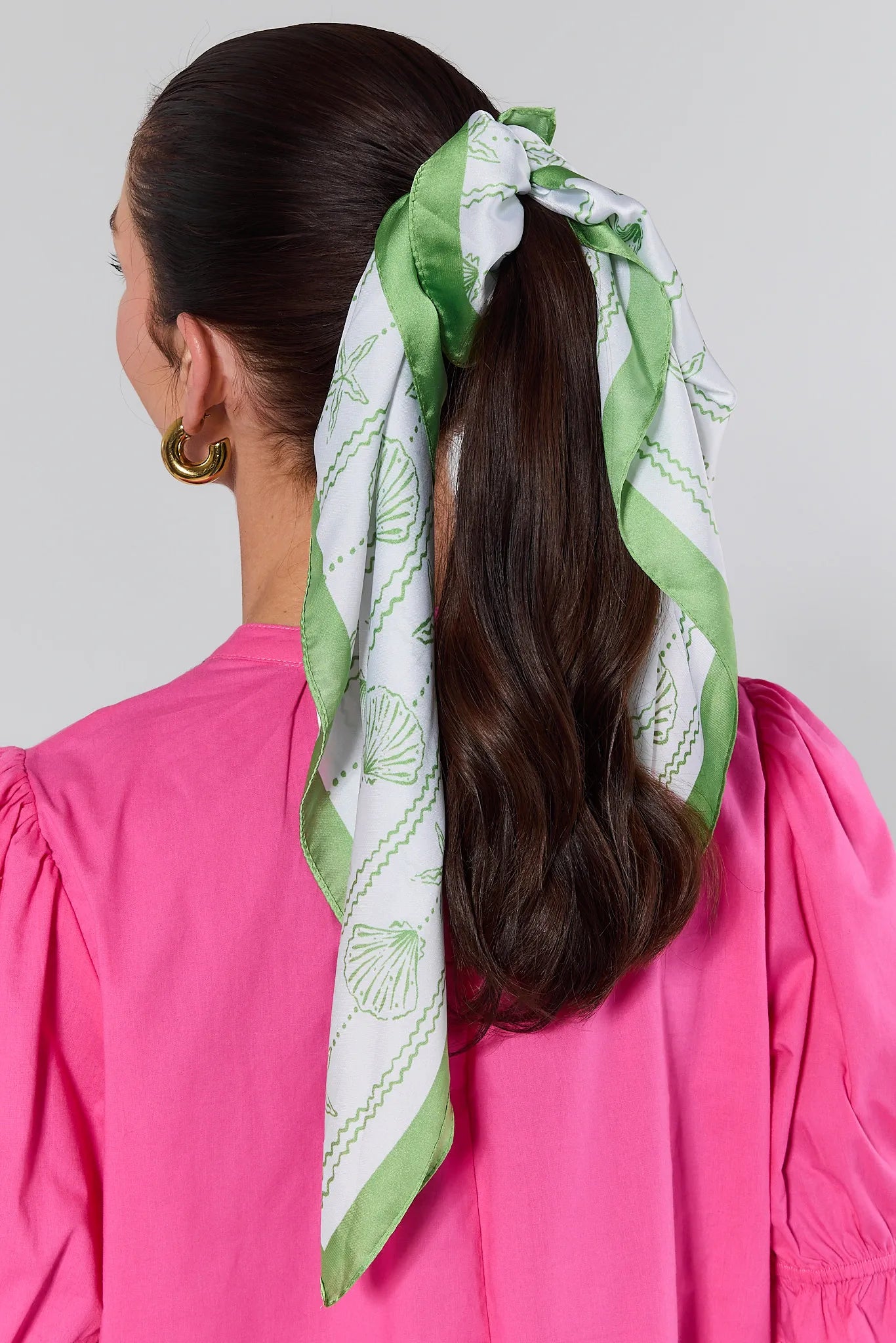 Person with a green and white patterned headscarf tied in a ponytail against a gray background