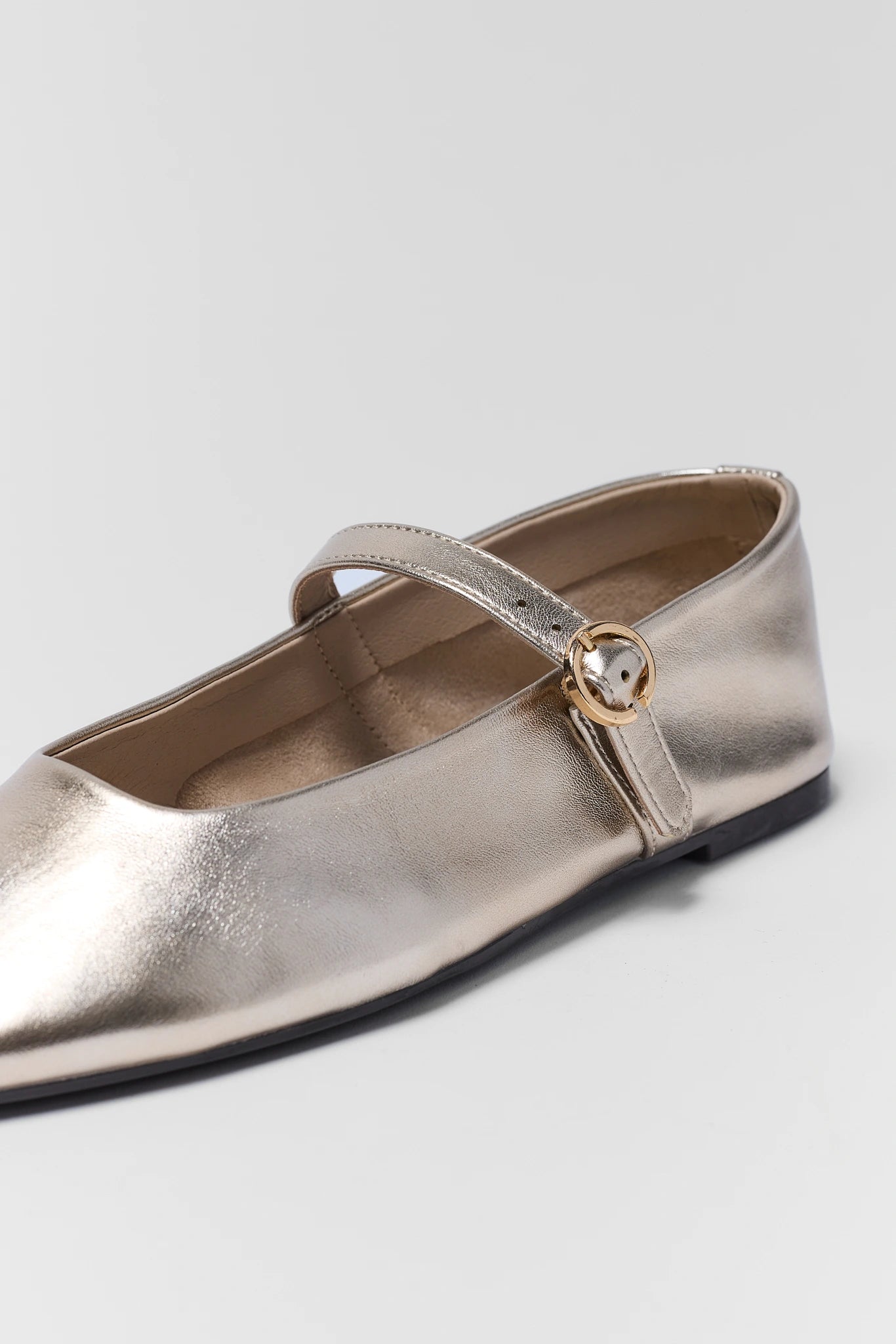 Gold metallic flat shoe with a strap on a light gray background