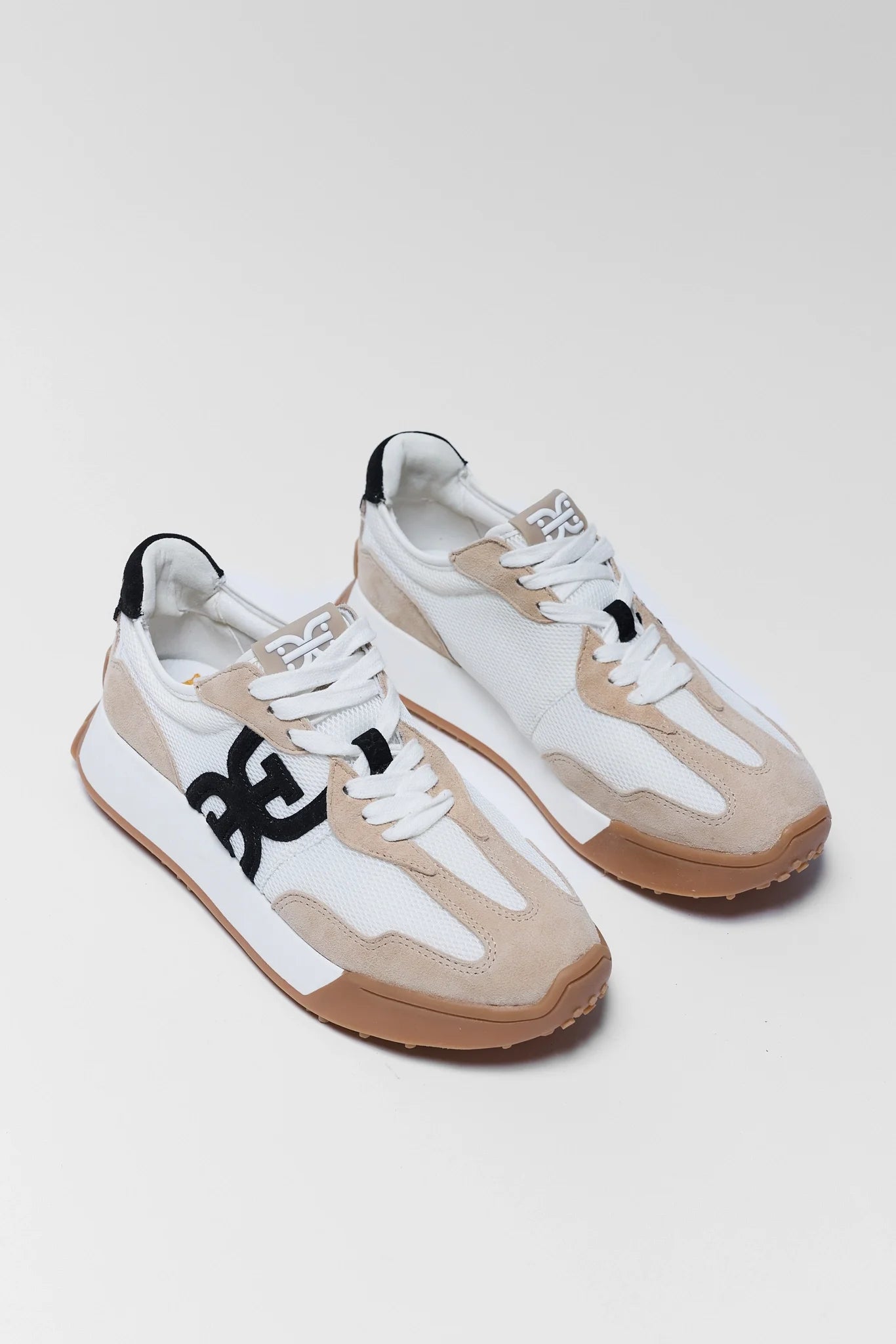 Pair of white and beige sneakers with black accents on a light gray background