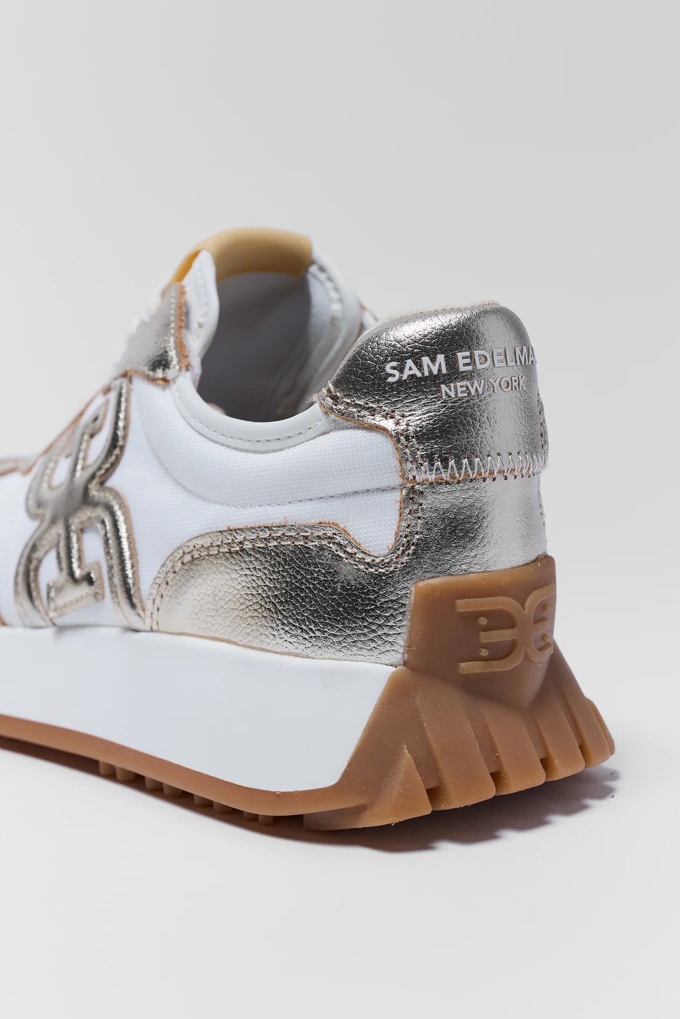 White and silver sneaker with brown sole on a light gray background