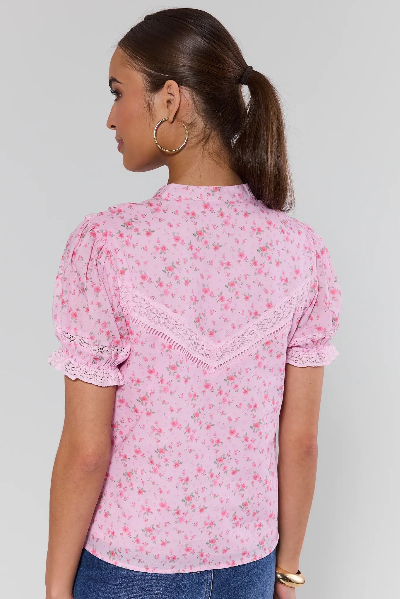 Woman wearing a pink floral blouse with lace details on a plain background