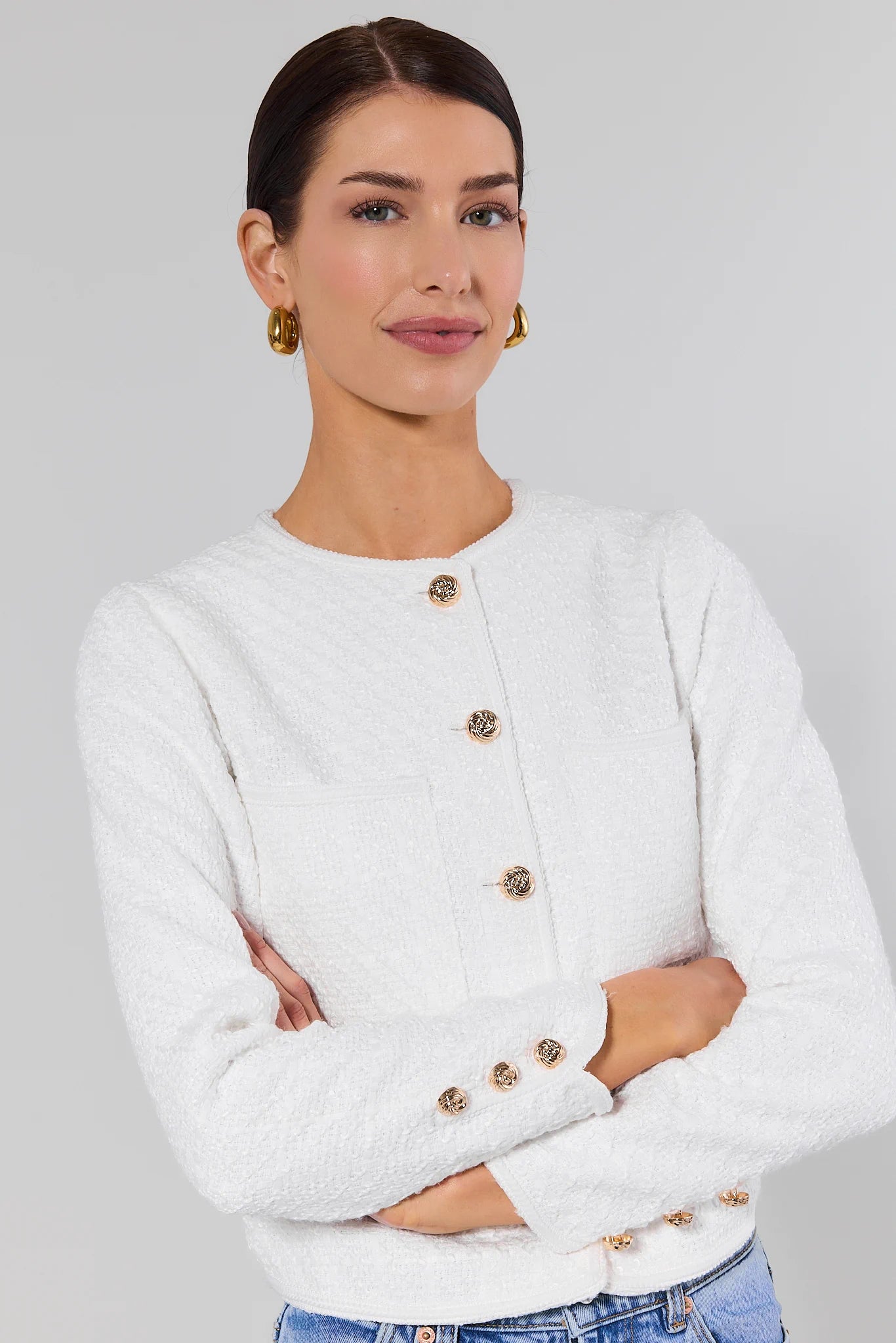 Woman wearing a white cardigan with gold buttons on a gray background