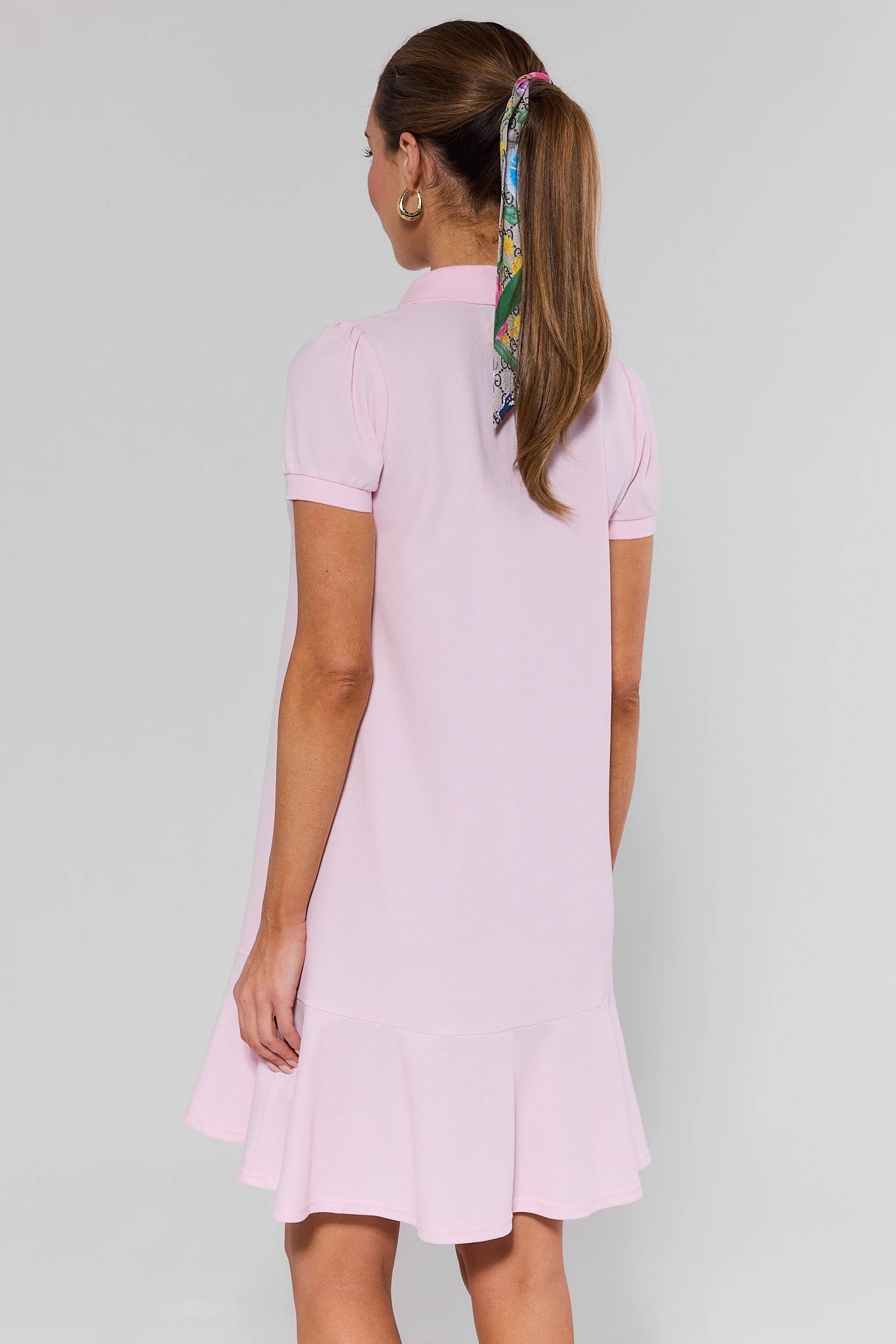 Woman wearing a pink dress with a patterned headscarf on a gray background