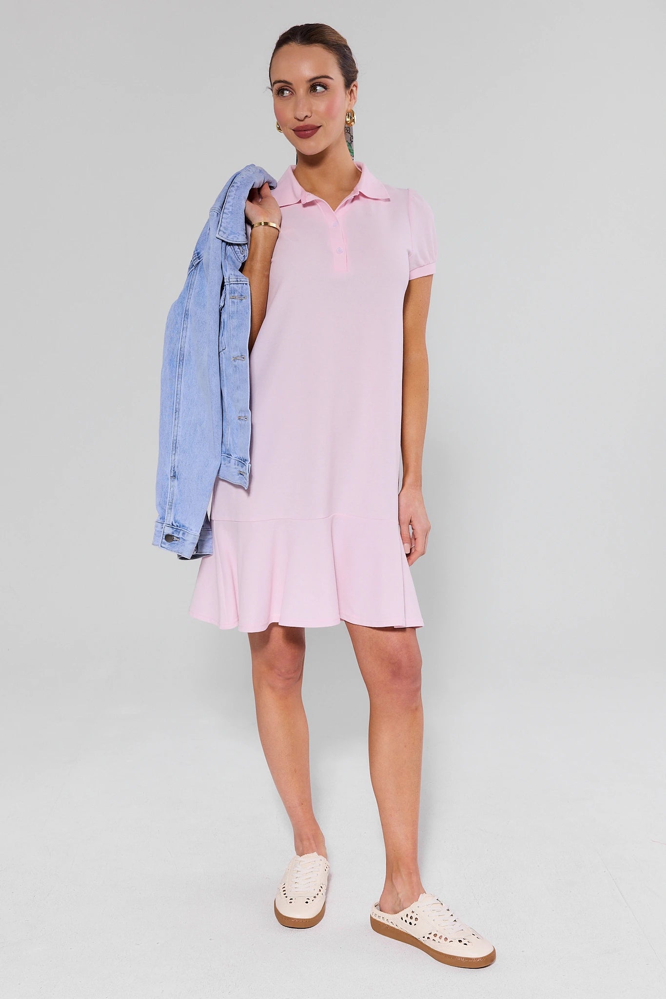 Woman wearing a pink dress with a denim jacket over her shoulder on a plain background