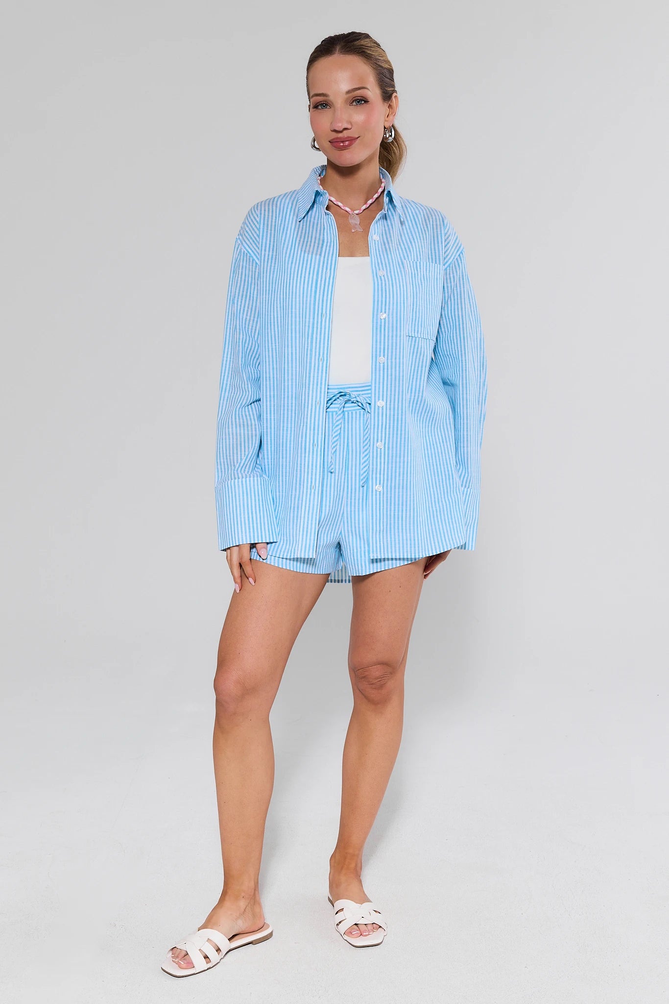 Woman wearing a light blue striped shirt and shorts on a white background