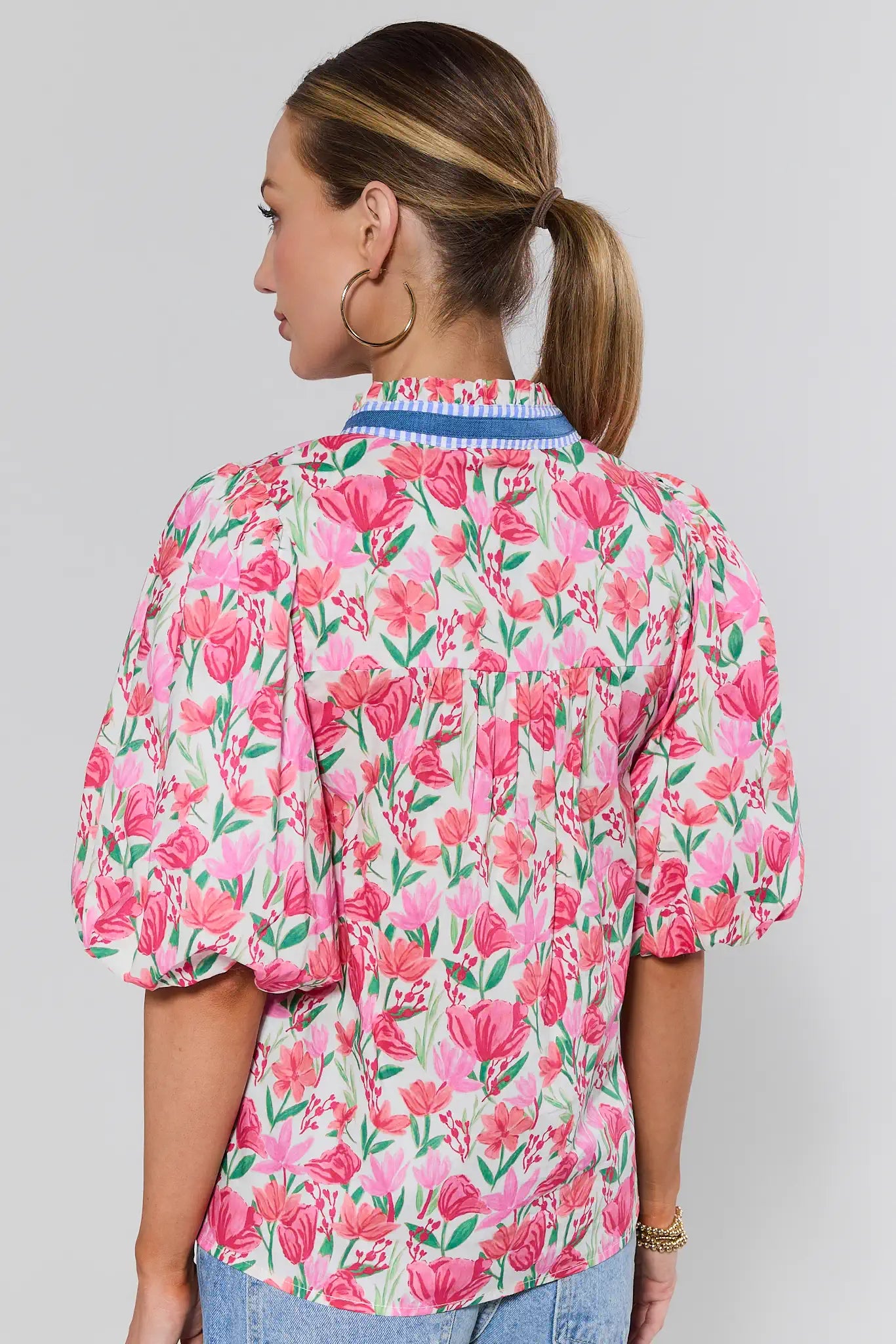 Woman wearing a pink floral blouse and jeans against a plain background