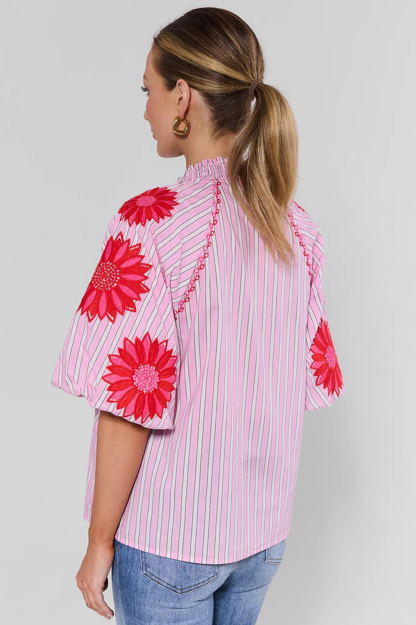 Woman wearing a pink blouse with red patterns on a plain background