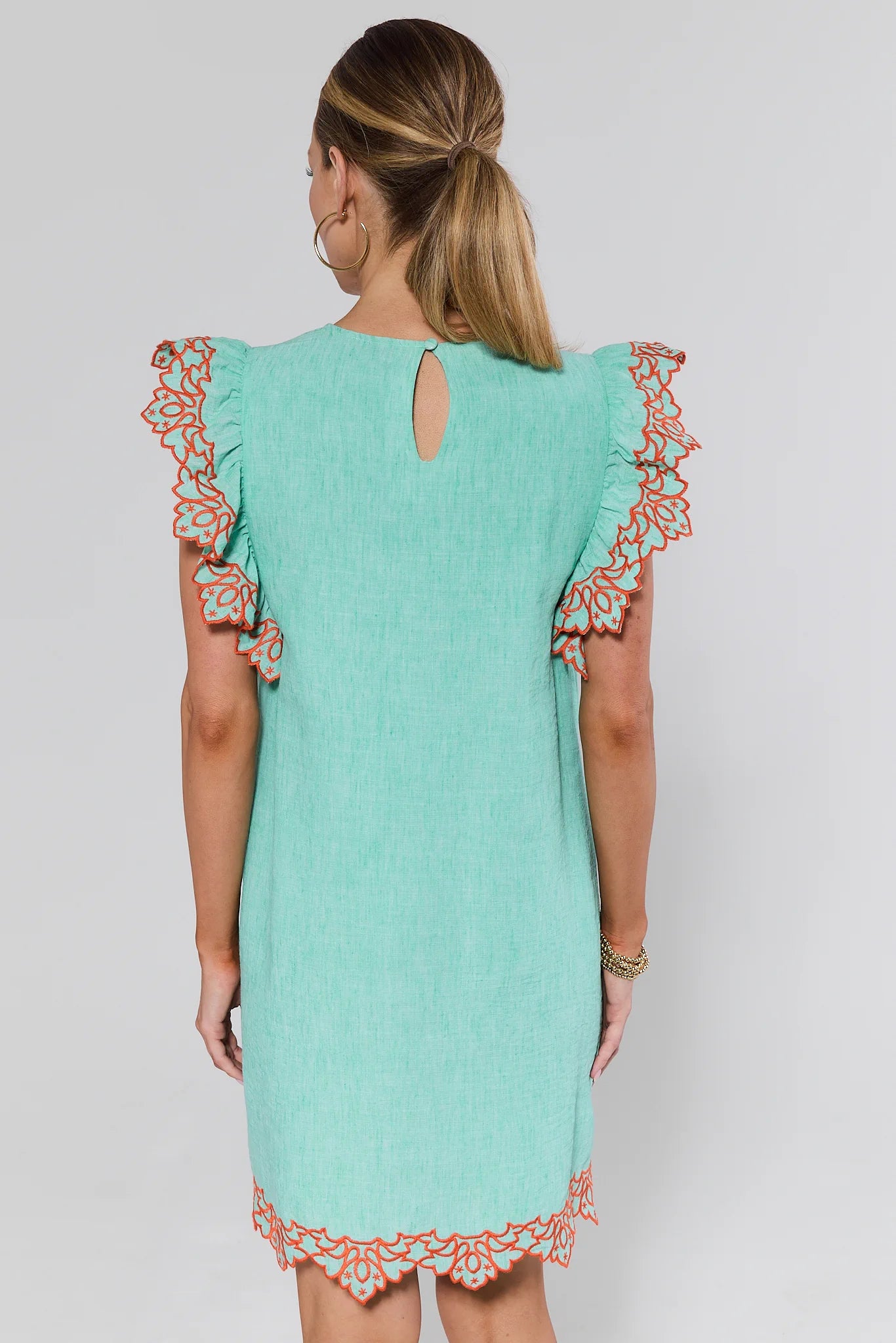 Woman wearing a turquoise dress with floral lace details on sleeves and hem against a white background