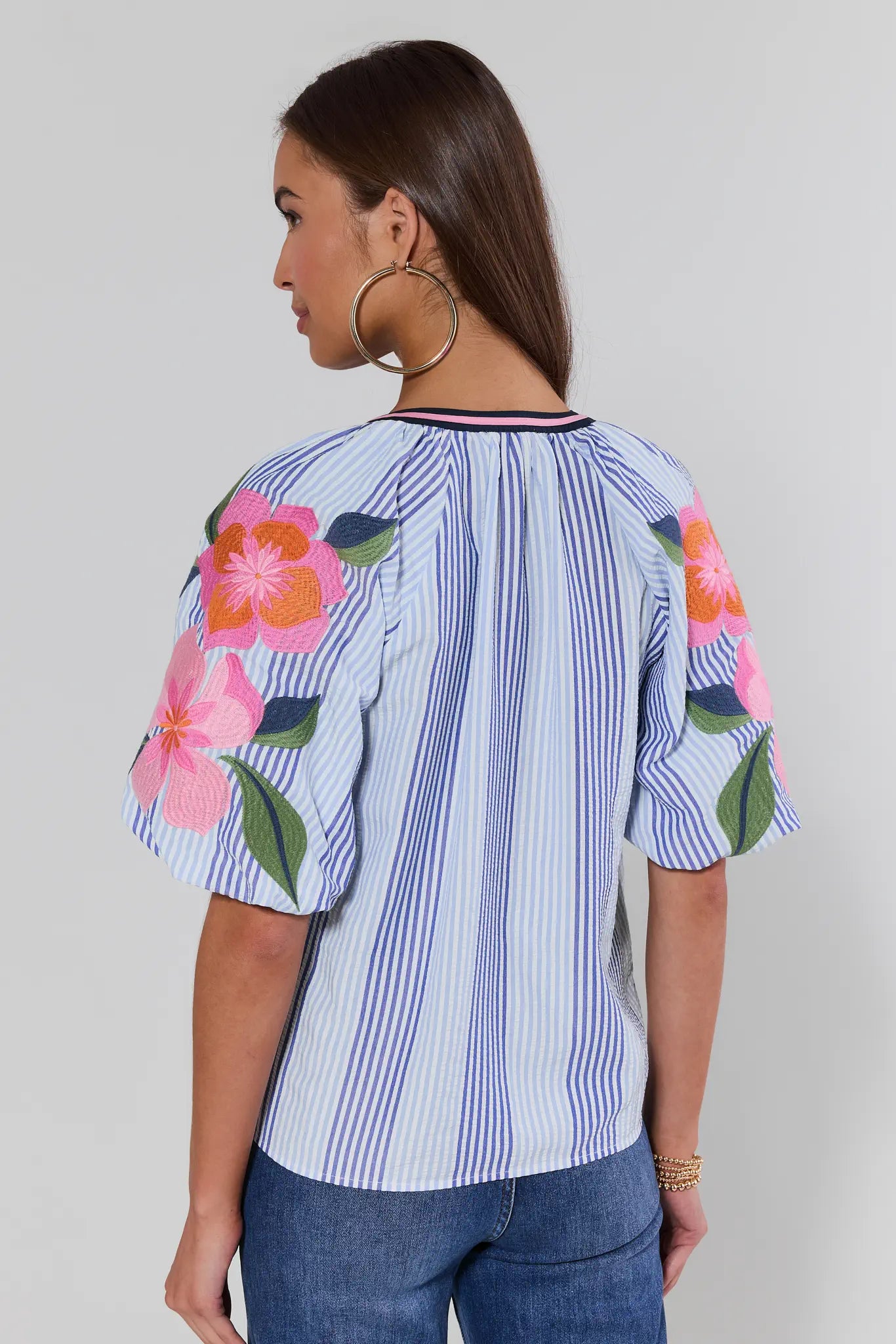 Woman wearing a blue and white striped shirt with floral sleeves on a plain background