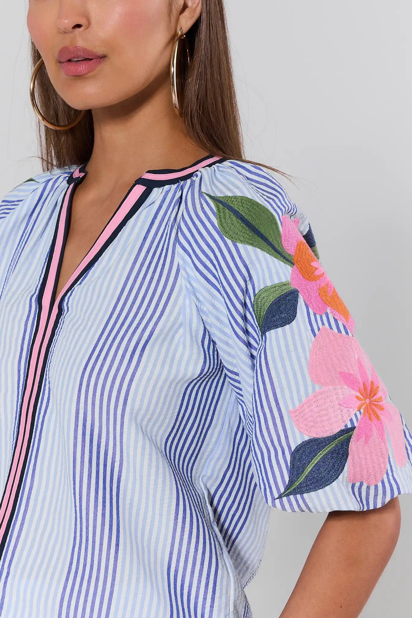 Woman wearing a blue and white striped shirt with floral sleeves on a plain background