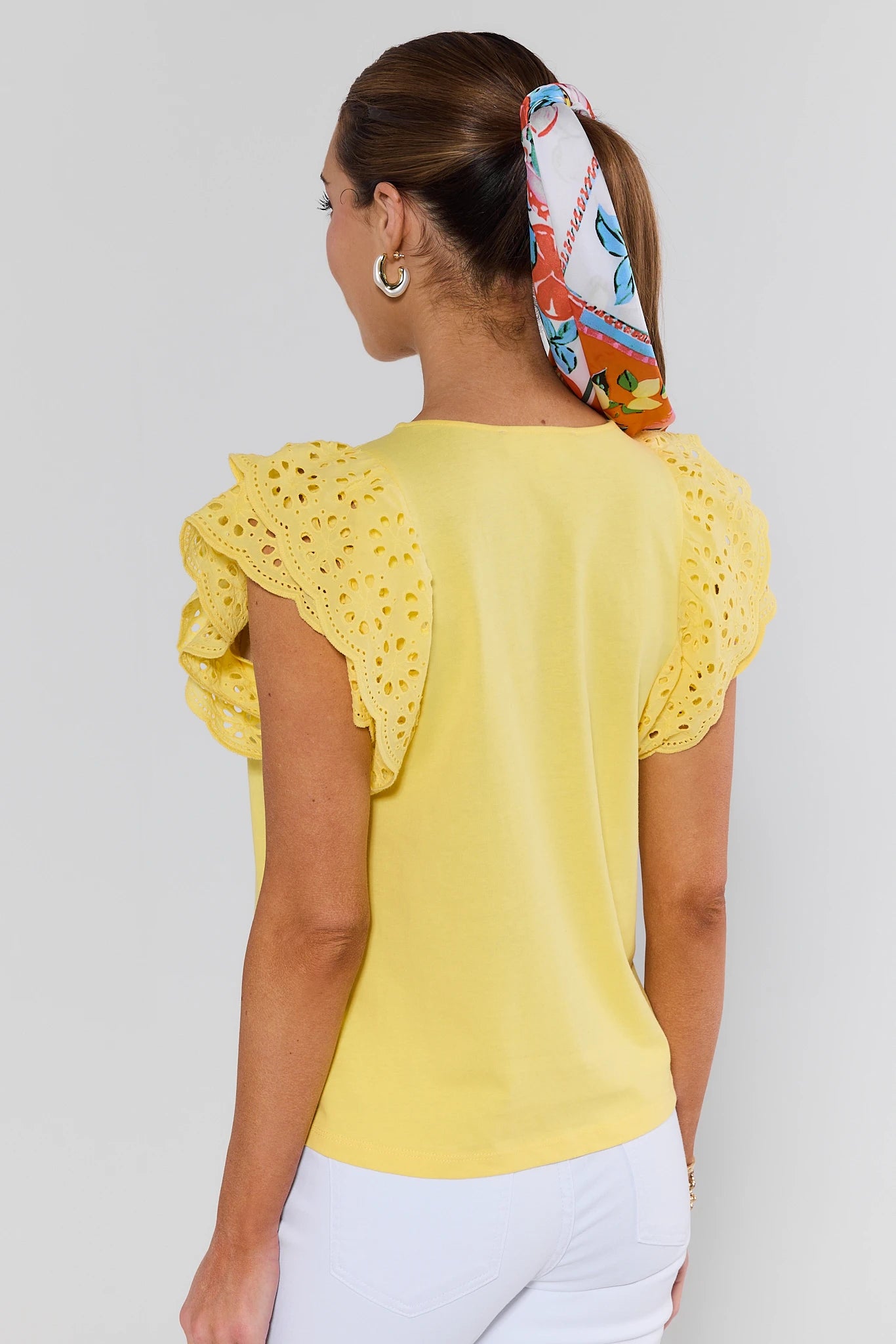 Woman wearing a yellow top with lace sleeves and a colorful headscarf on a white background