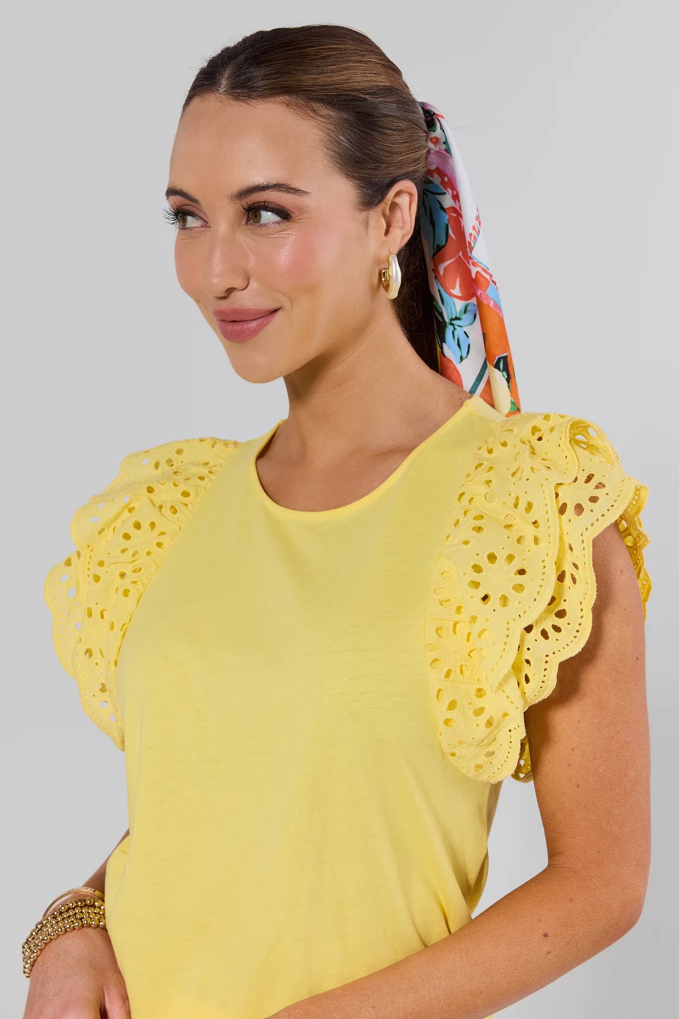 Woman wearing a yellow top with ruffled sleeves against a gray background