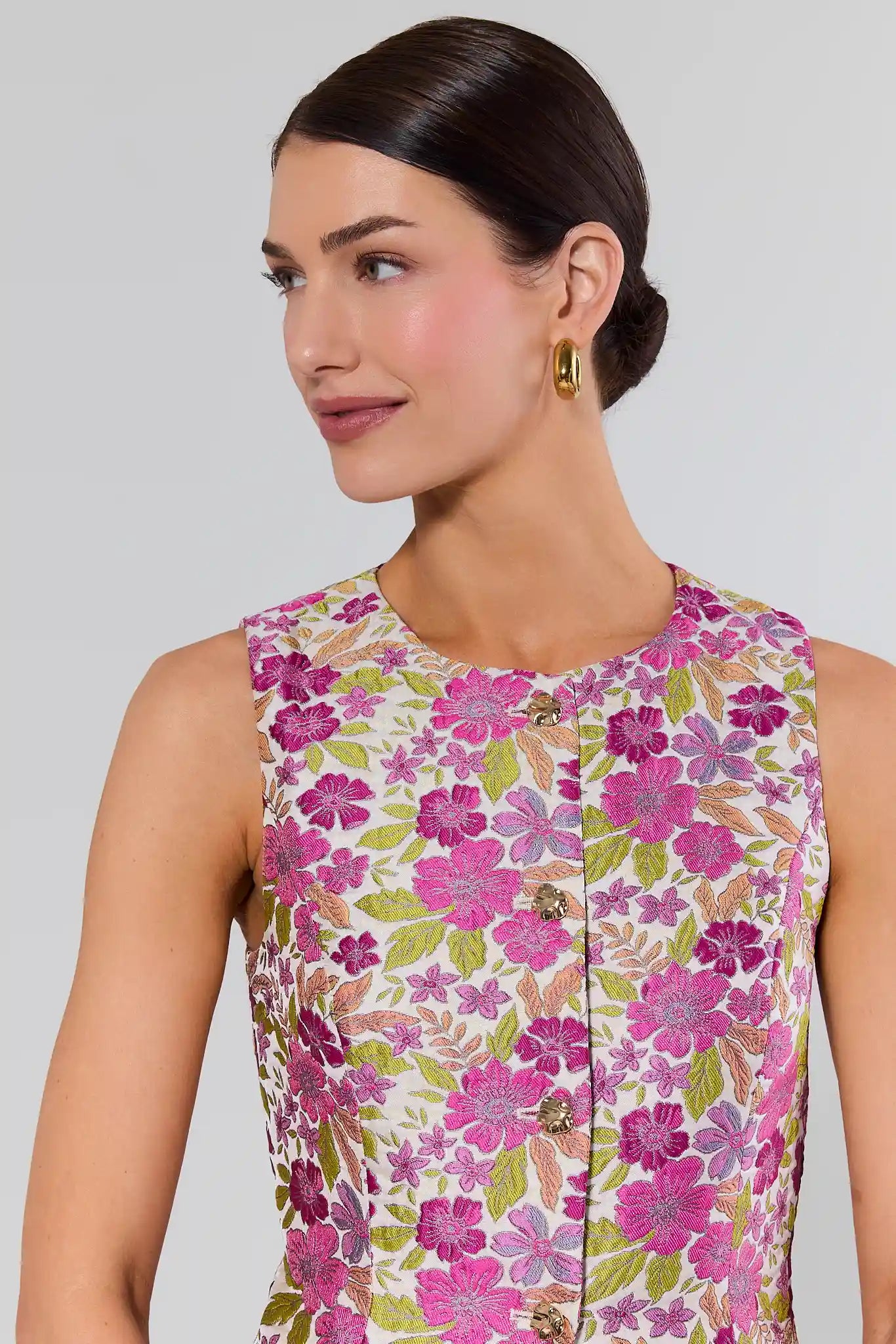 close up Woman wearing a sleeveless floral top with pink and green flowers on a plain background