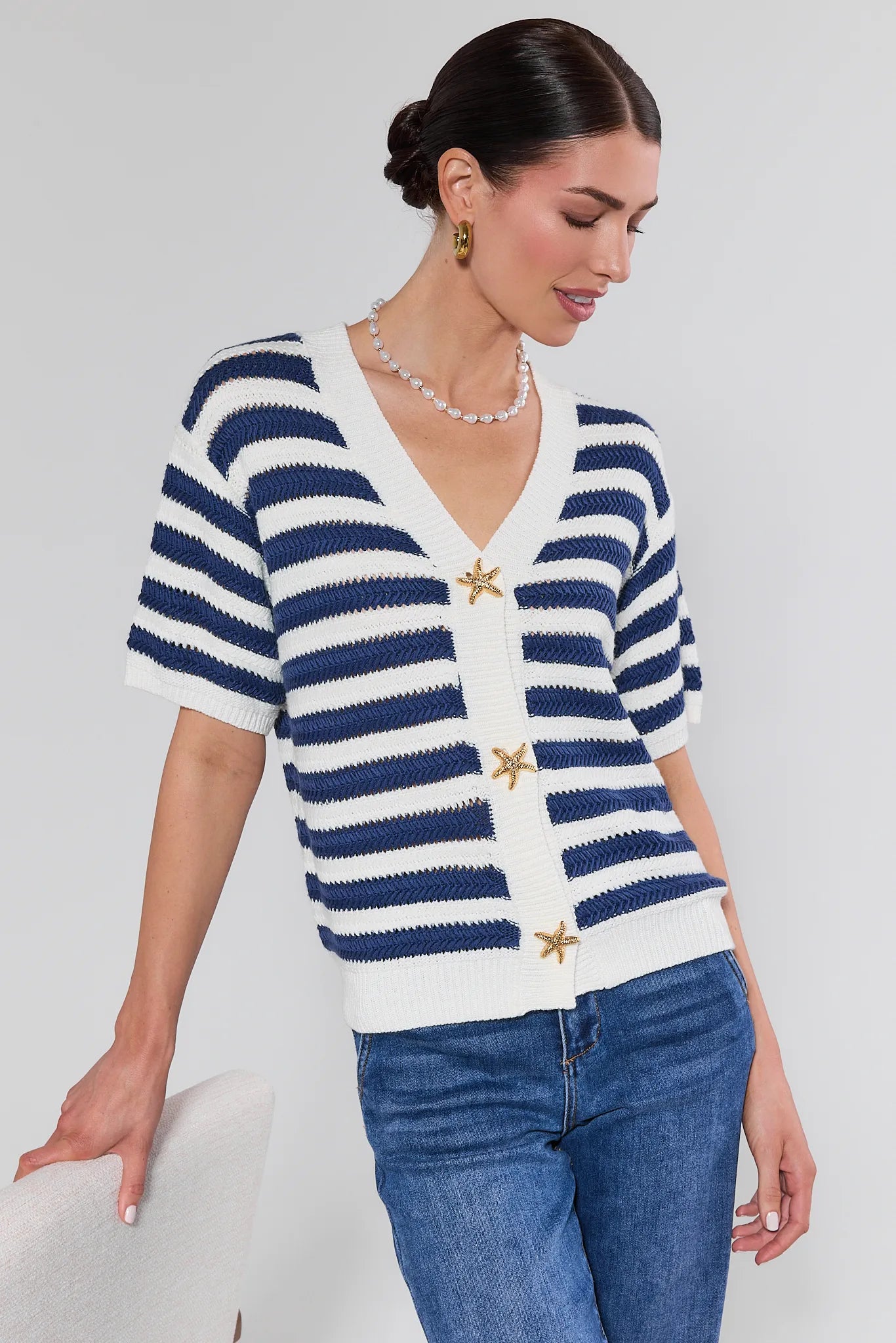 Woman wearing a blue and white striped cardigan with star details on a plain background