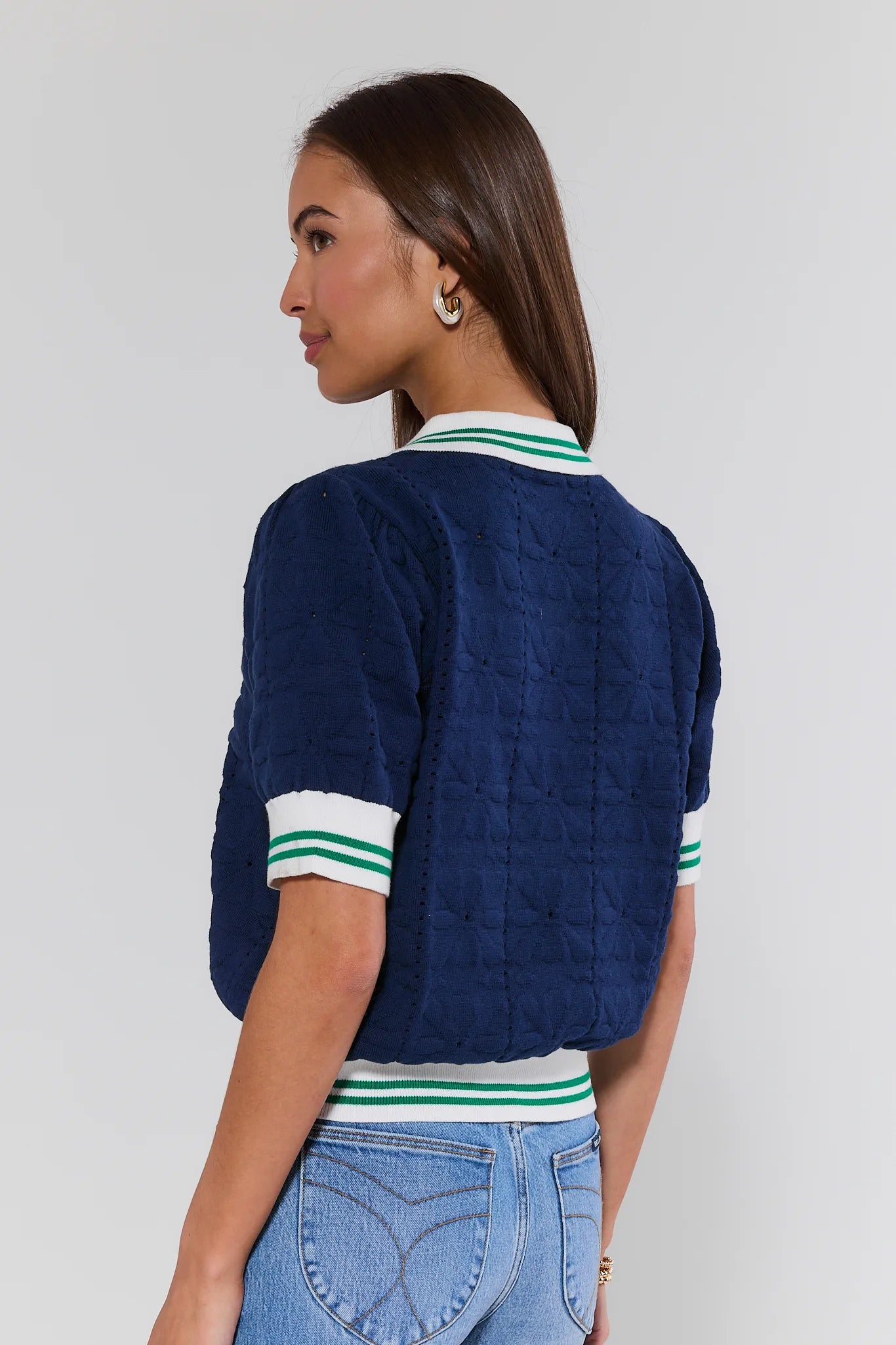 Woman wearing a navy blue quilted jacket with white and green trim on a plain background