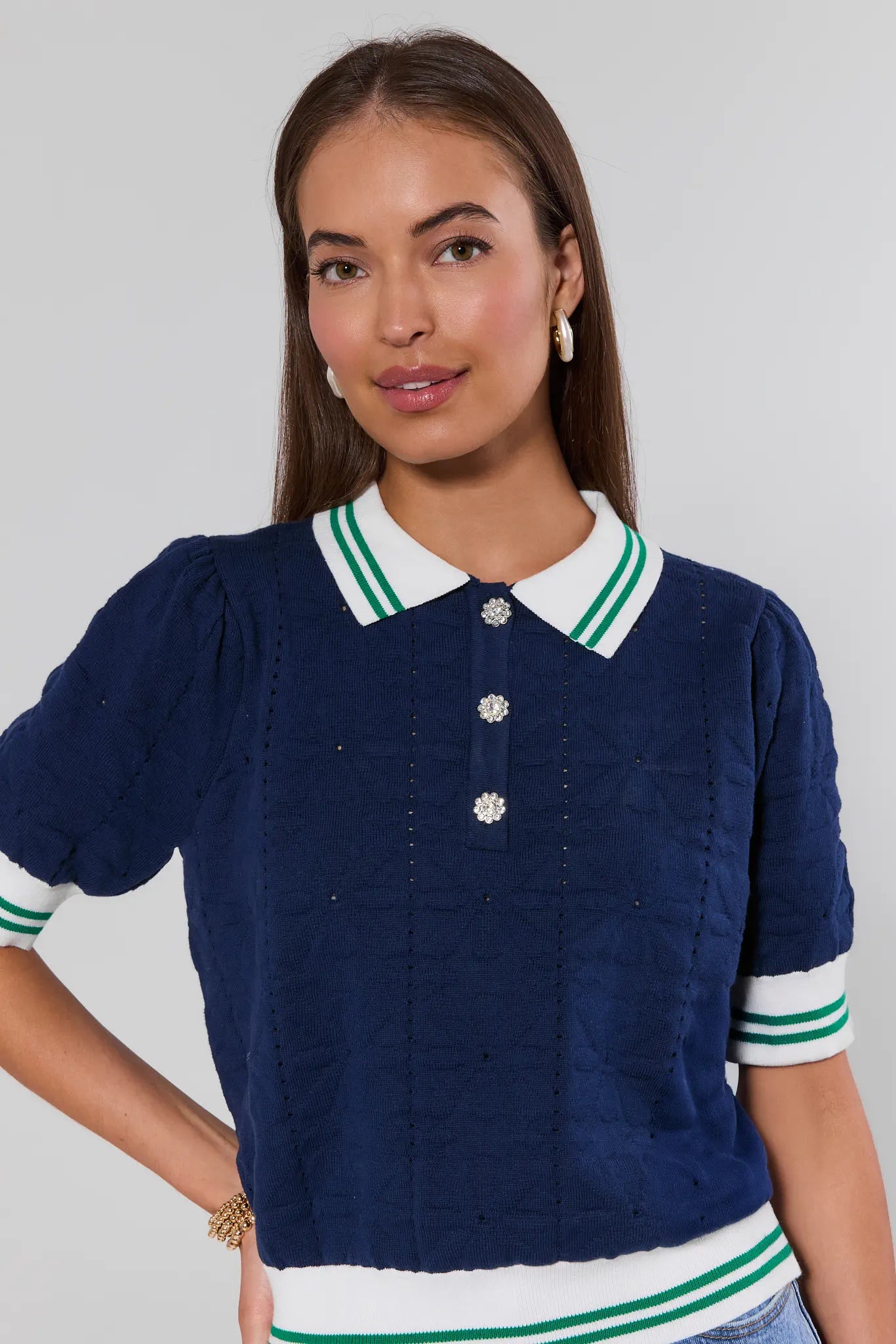 Woman wearing a navy blue sweater with white and green trim on a gray background