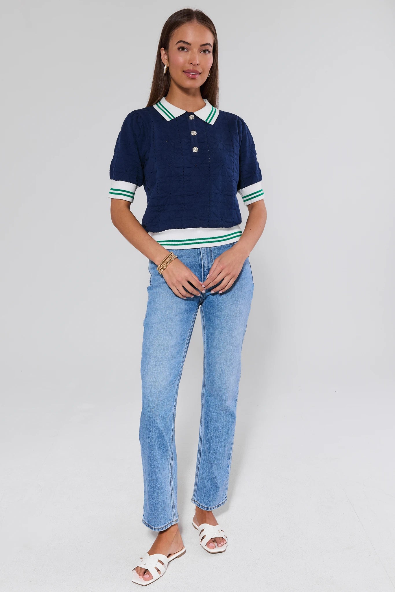 Woman wearing a navy polo shirt with white trim and light blue jeans on a gray background