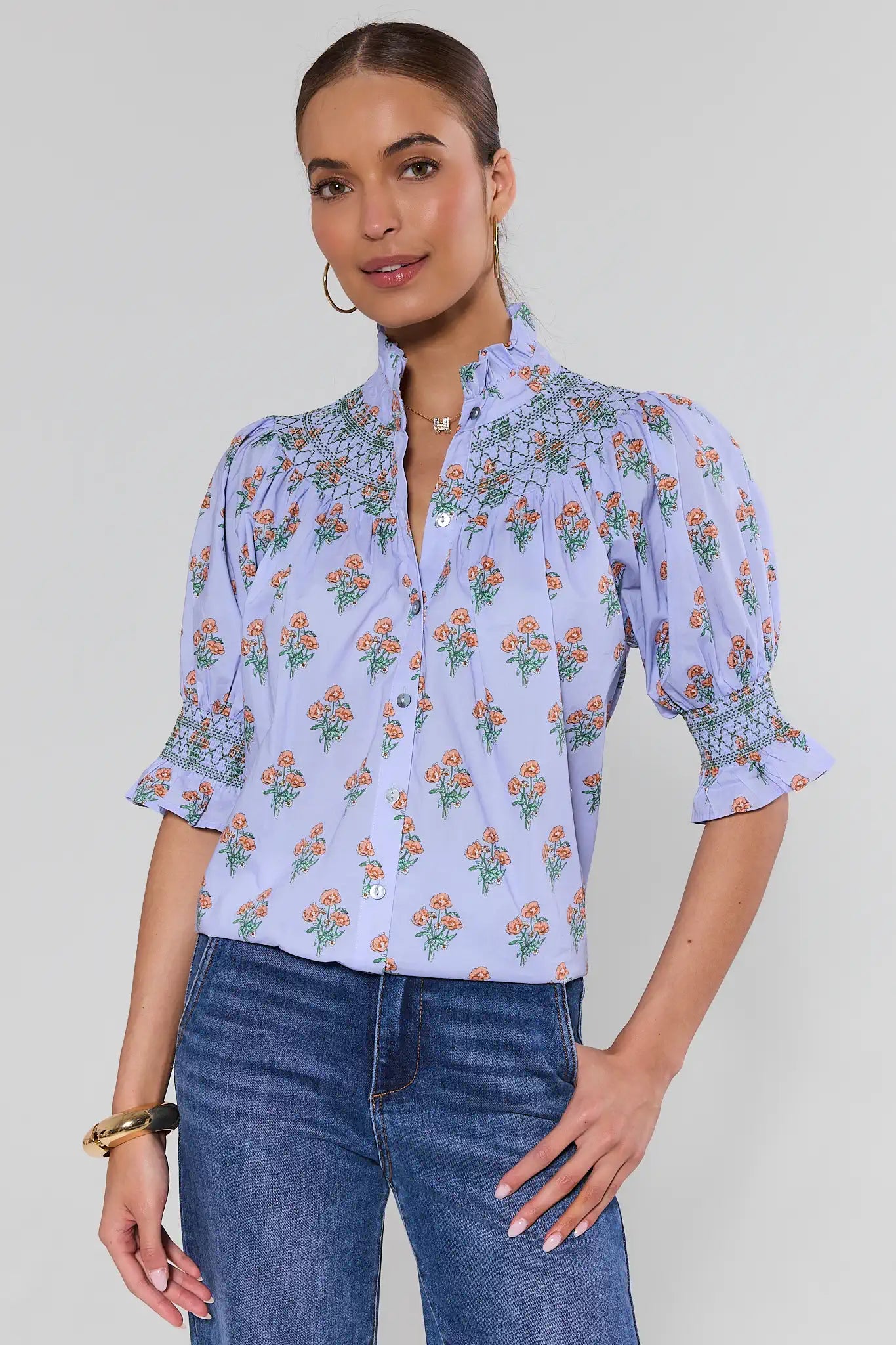 Woman wearing a floral blouse and jeans on a plain background