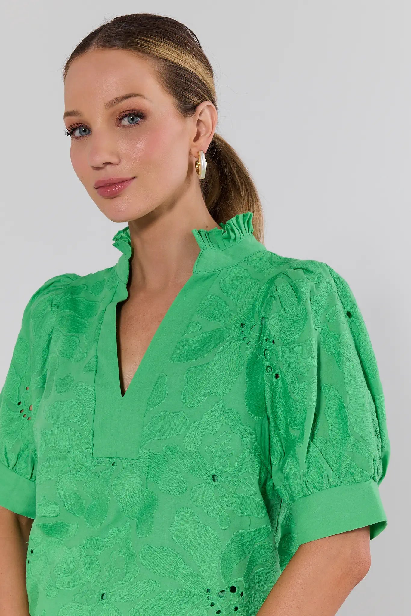 Woman wearing a green blouse with puff sleeves against a plain background
