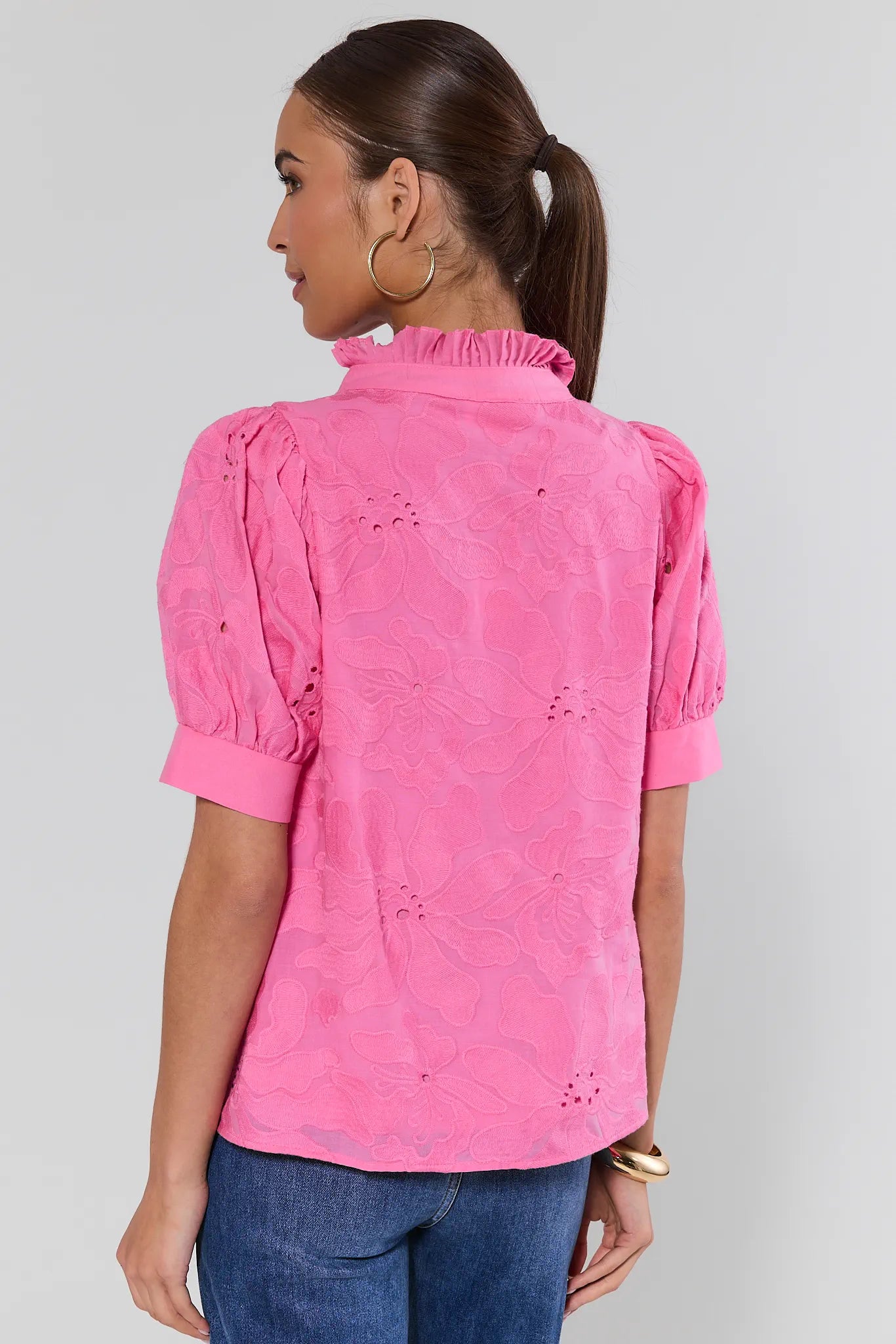 Woman wearing a pink blouse with short sleeves and blue jeans on plain background