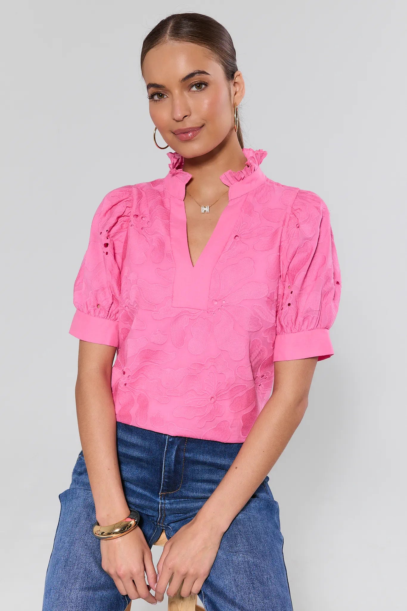 Woman wearing a pink blouse with puffed sleeves and blue jeans on a plain background