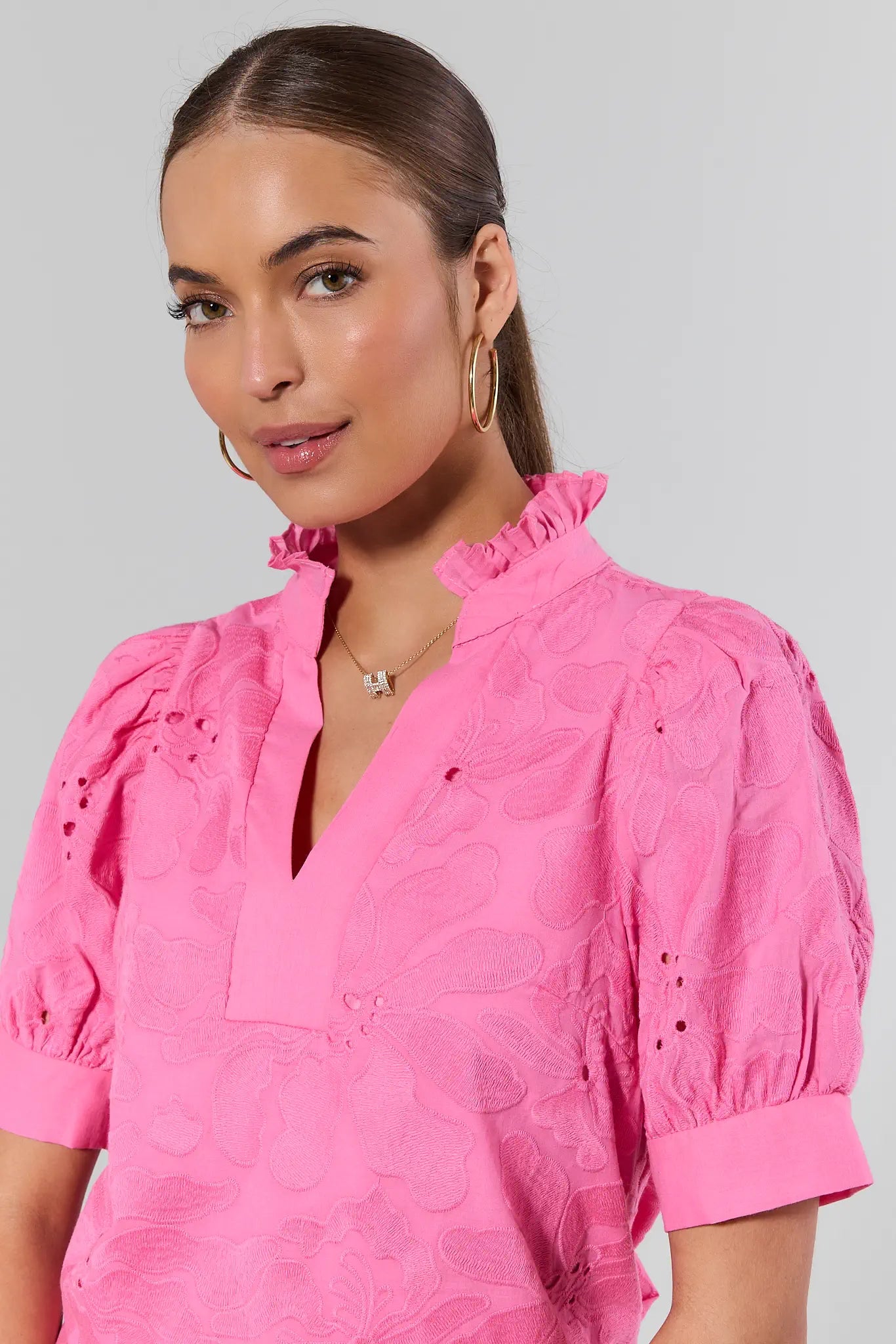 Woman wearing a bright pink blouse with ruffled collar and short sleeves against a plain background